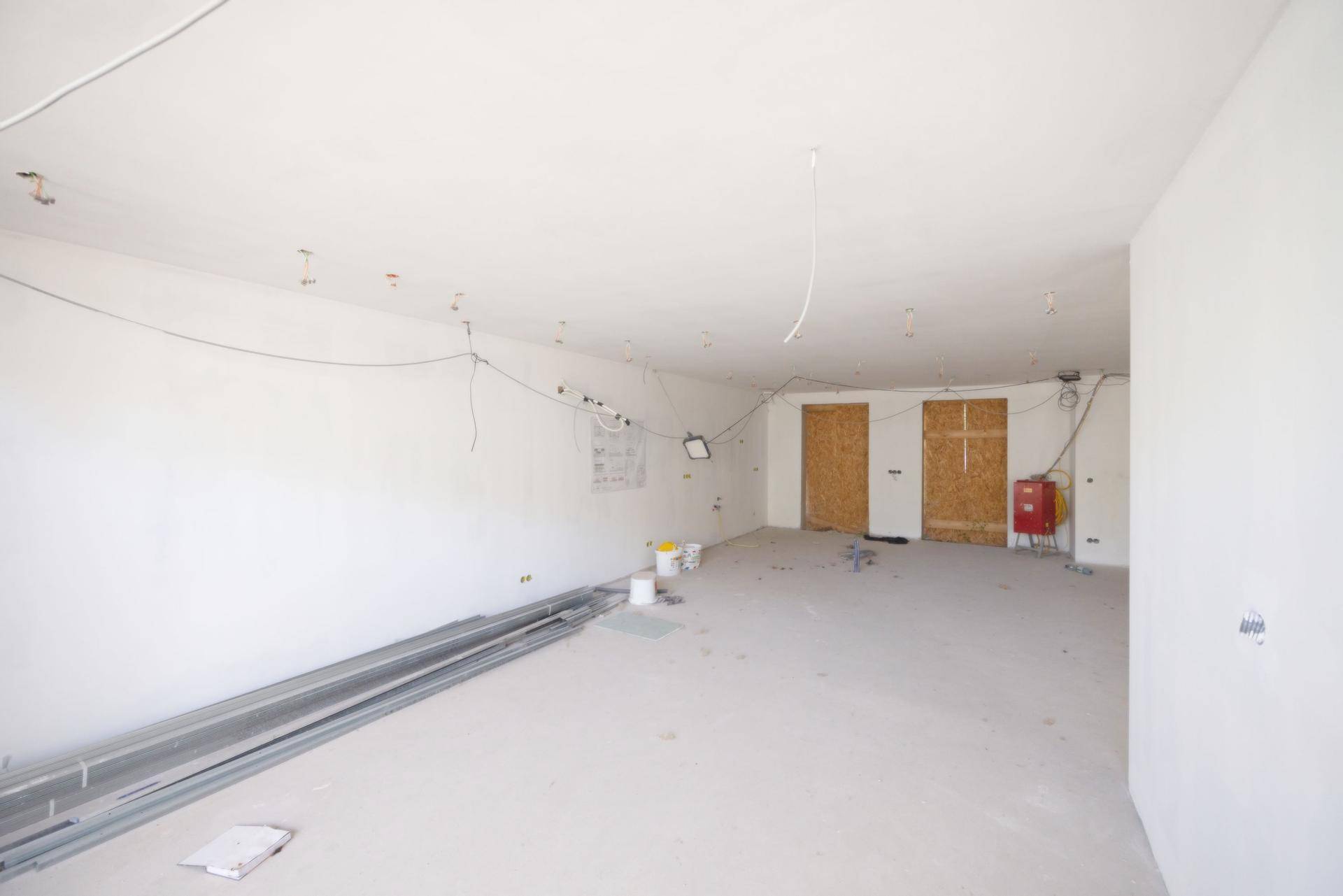 Unfertiger Innenraum mit zwei verschlossenen Türöffnungen und Installationsmaterial am Boden.