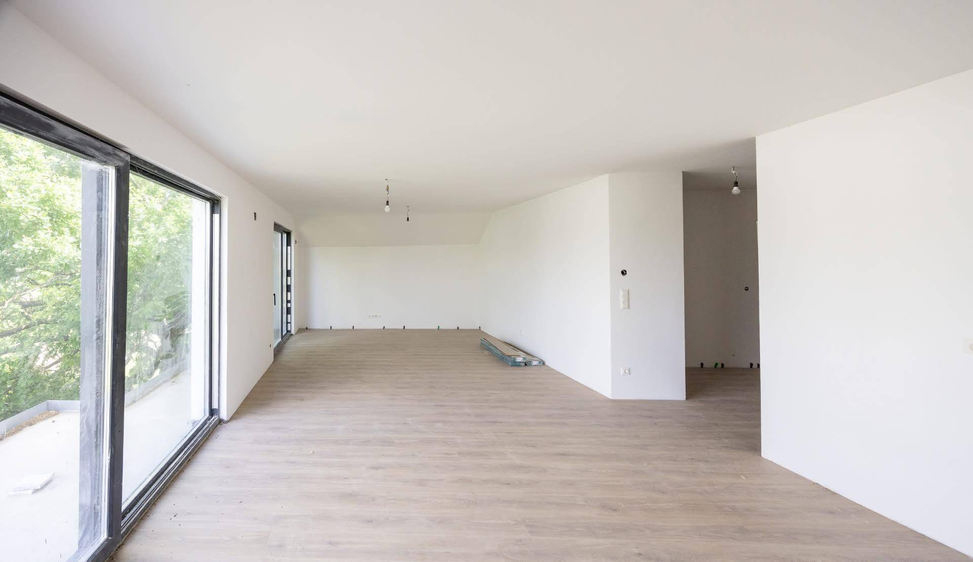 Heller Wohnbereich im Rohbau mit großen Schiebetüren und neu verlegtem Laminatboden.