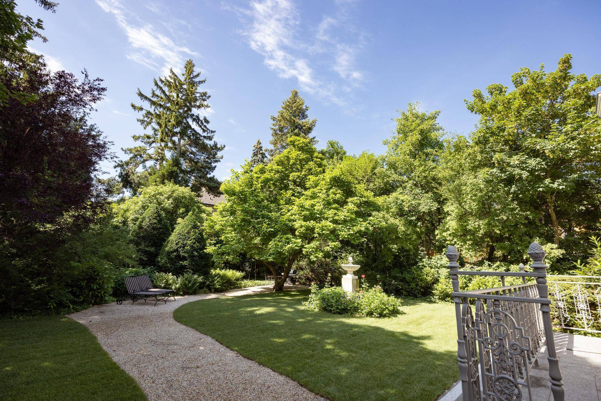 Weitläufiger Garten mit altem Baumbestand, Kieswegen und einer gemütlichen Sitzbank.