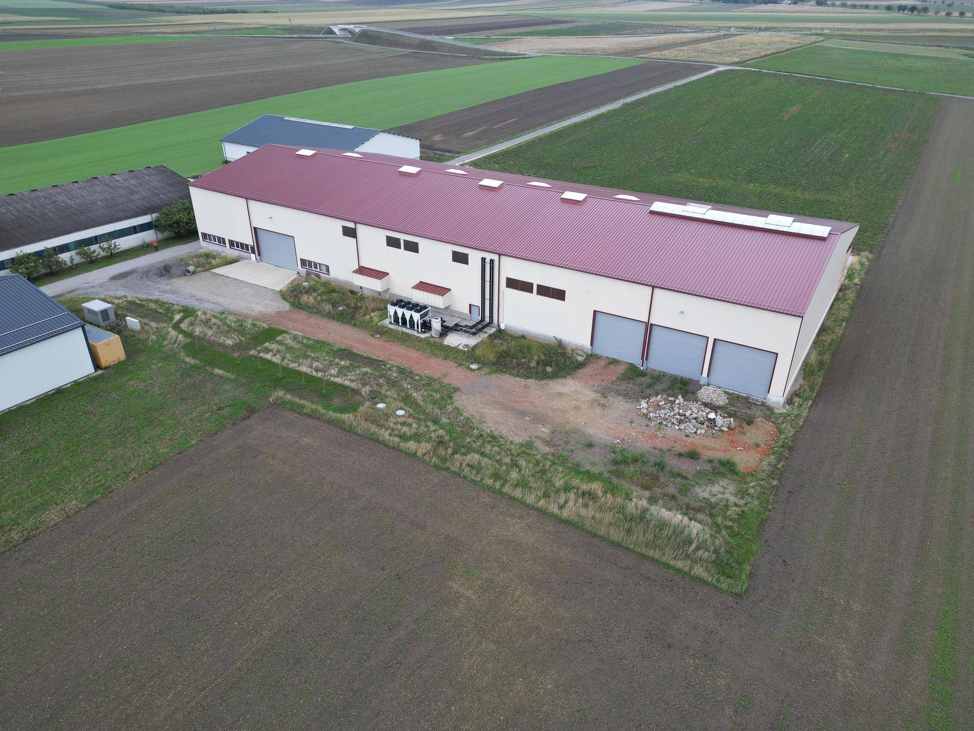 Weitläufige Luftansicht des Lagerhauses mit Laderampen und angrenzenden landwirtschaftlichen Flächen unter bewölktem Himmel.