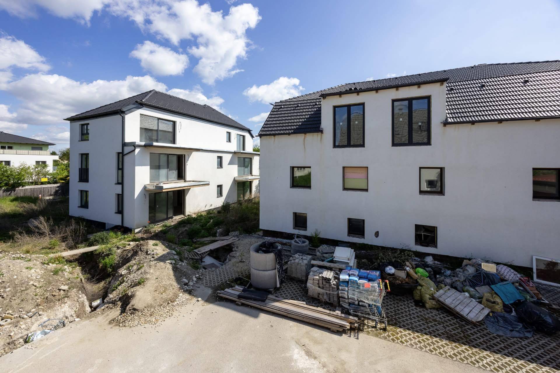 Zwei Neubauten in der Bauphase mit großen Fenstern und Baumaterialien im Vordergrund.