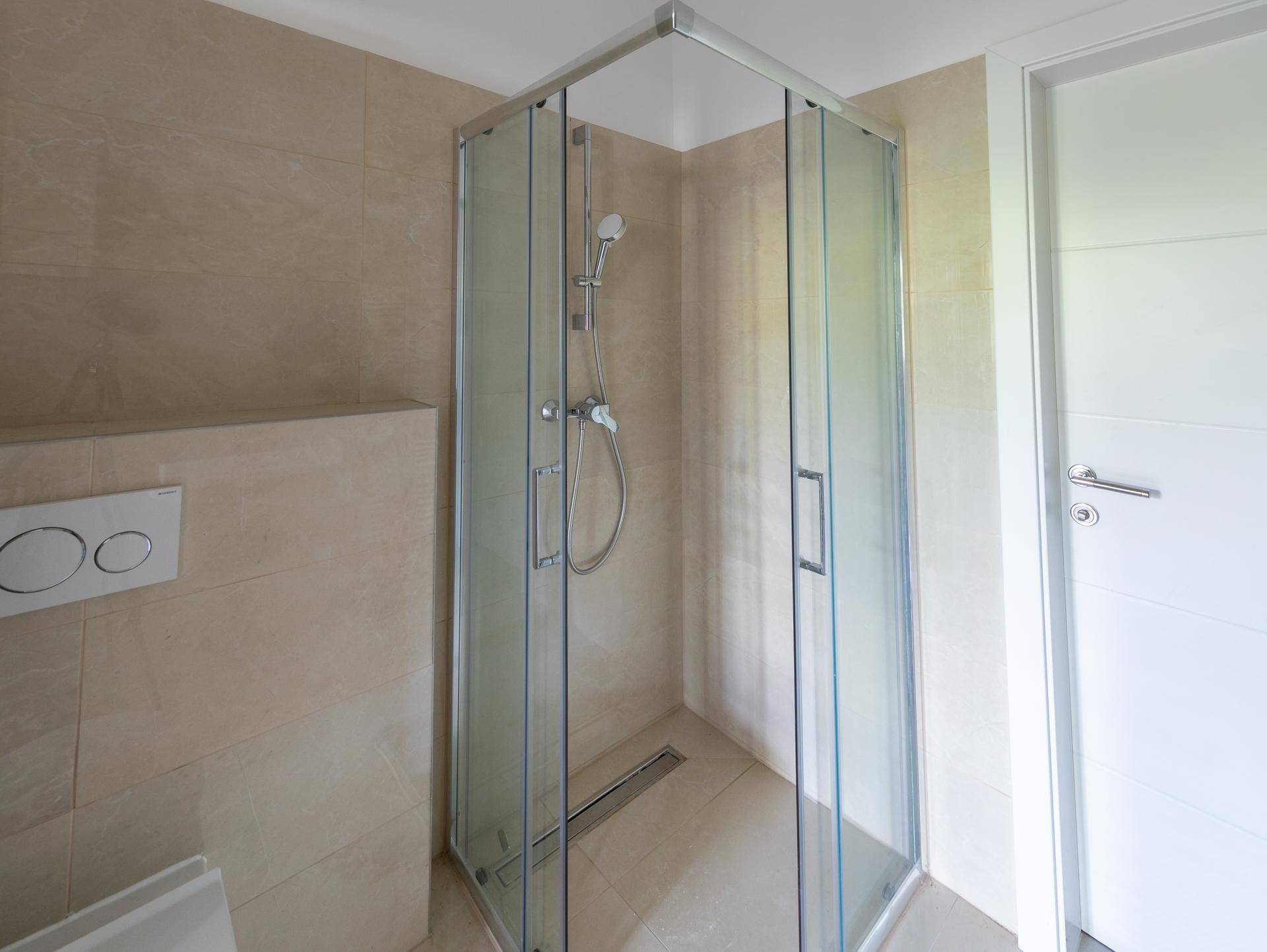 Modernes Badezimmer mit begehbarer Dusche, beigefarbenen Fliesen und wandhängendem WC.