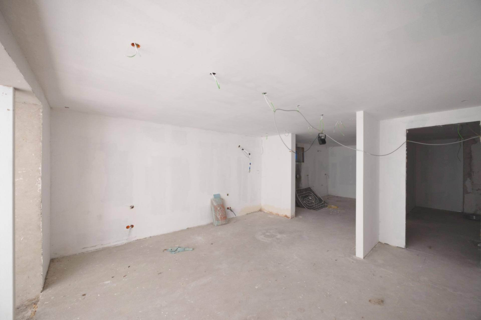 Leerer Raum im Rohbau mit weißen Wänden und Betonboden, bereit für den Innenausbau.