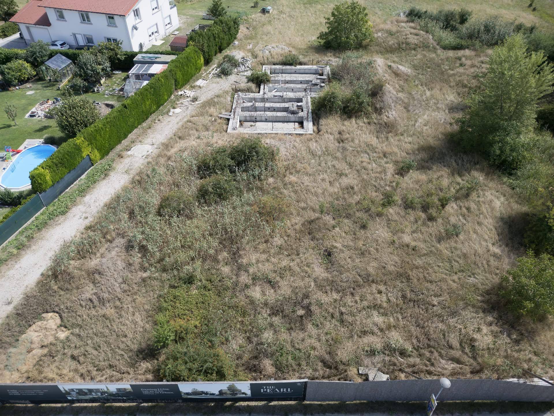 Nahaufnahme des Baugrundstücks aus der Luft mit deutlich sichtbaren Fundamenten und Werbebannern am Zaun.