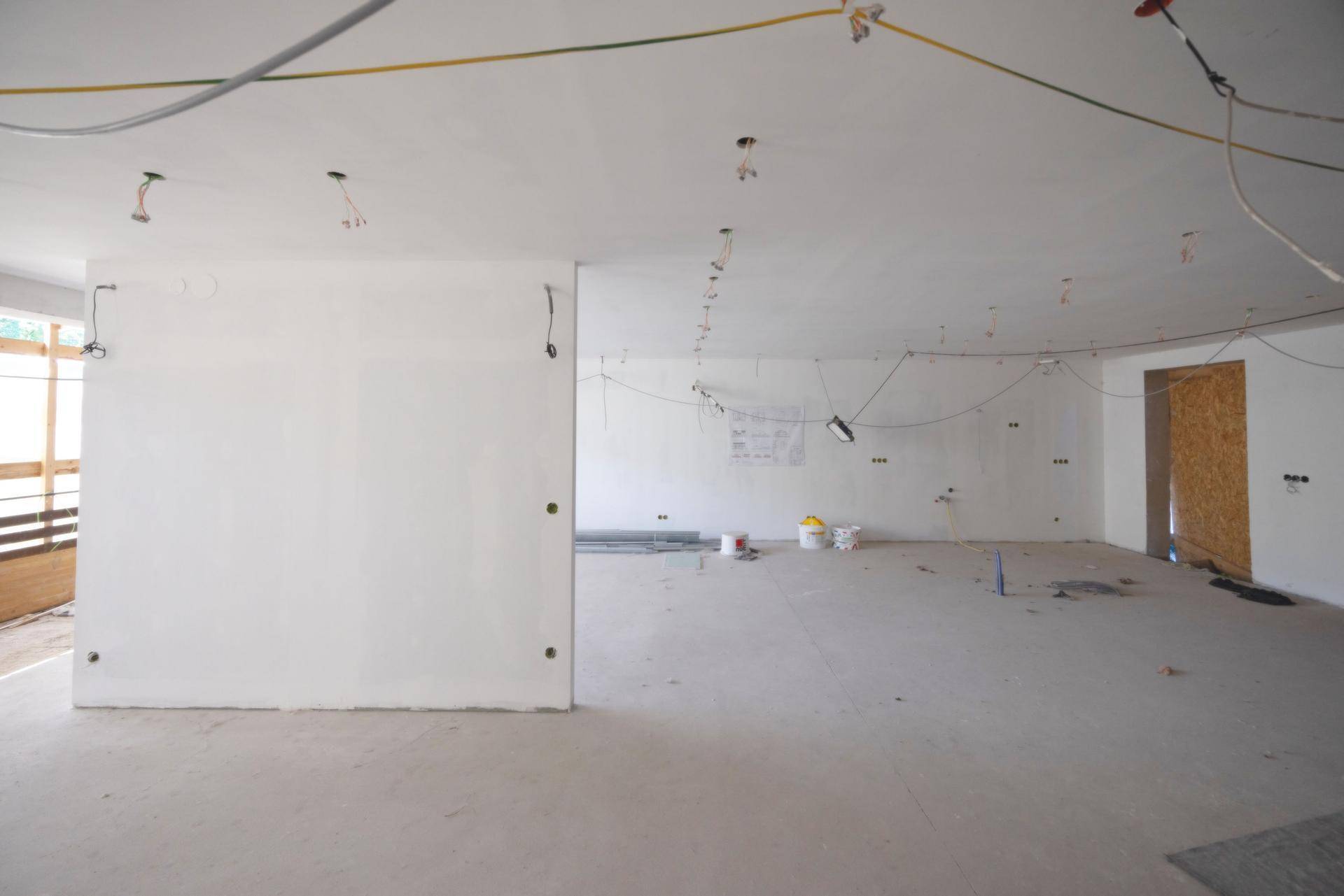 Großer, heller Raum im Rohbauzustand mit sichtbaren Elektroinstallationen und Betonboden.