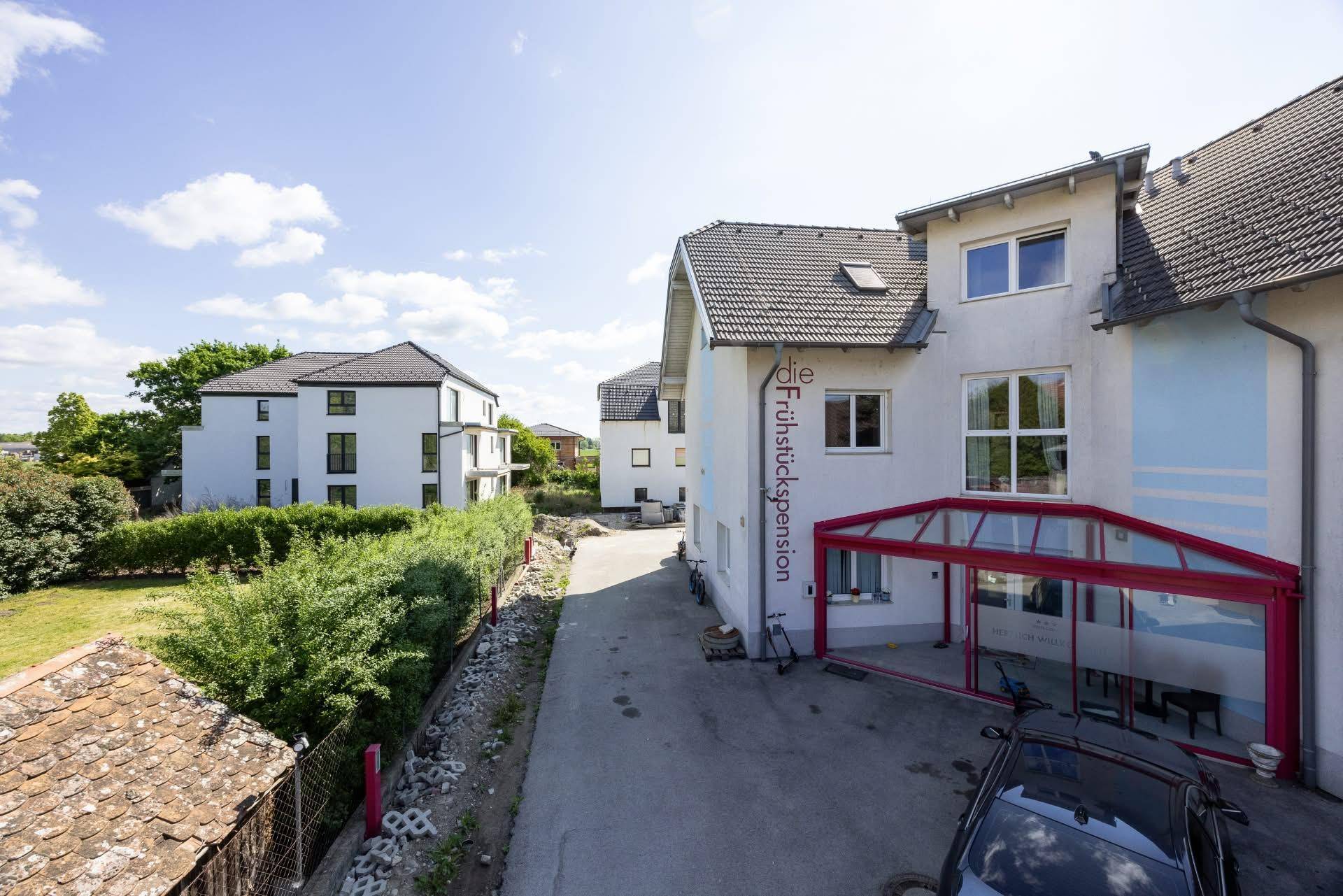 Ansicht eines Gebäudes mit rotem Wintergarten und einem geparkten Auto an einem sonnigen Tag.