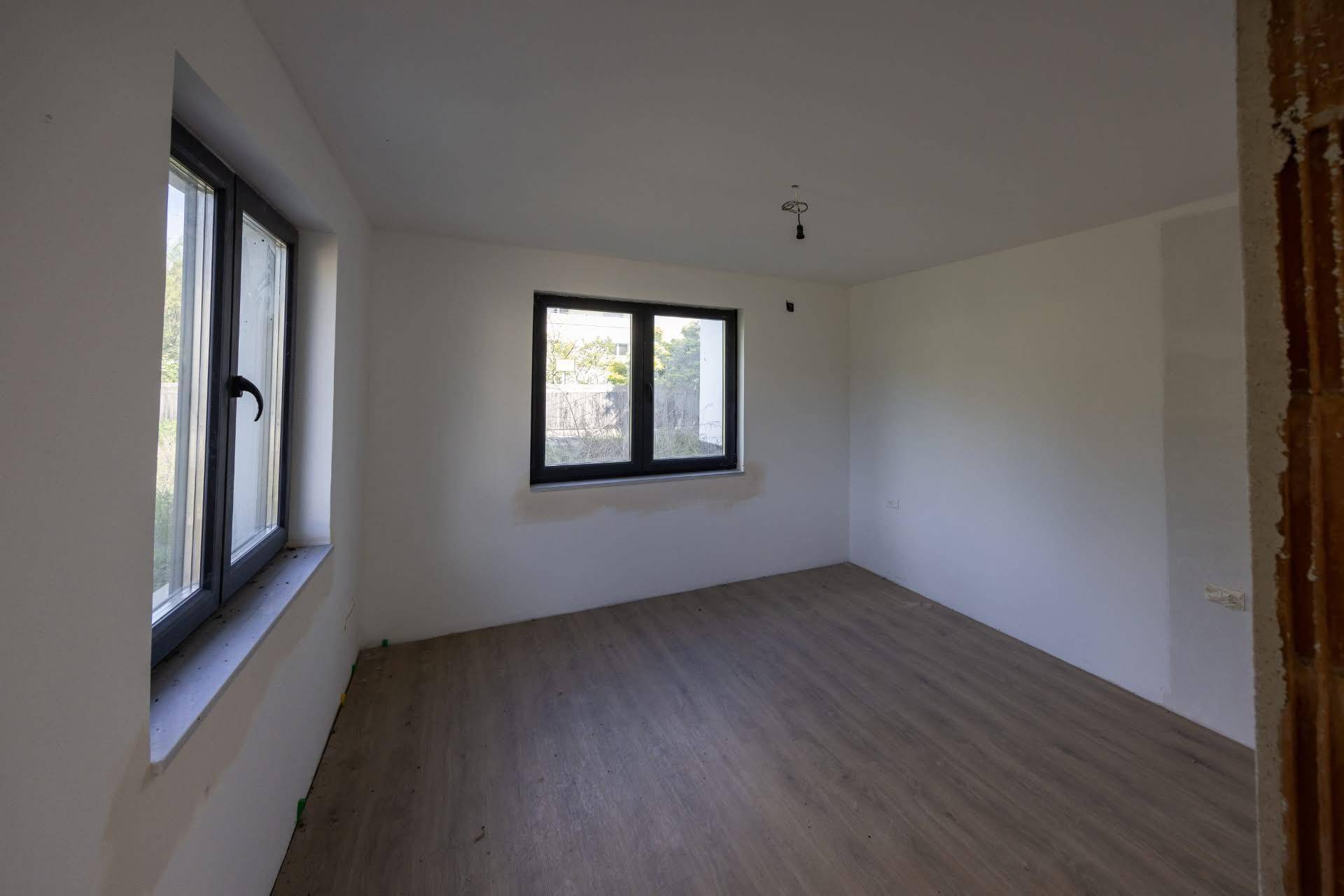 Helles Schlafzimmer im Rohbau mit zwei Fenstern und neu verlegtem Laminatboden.