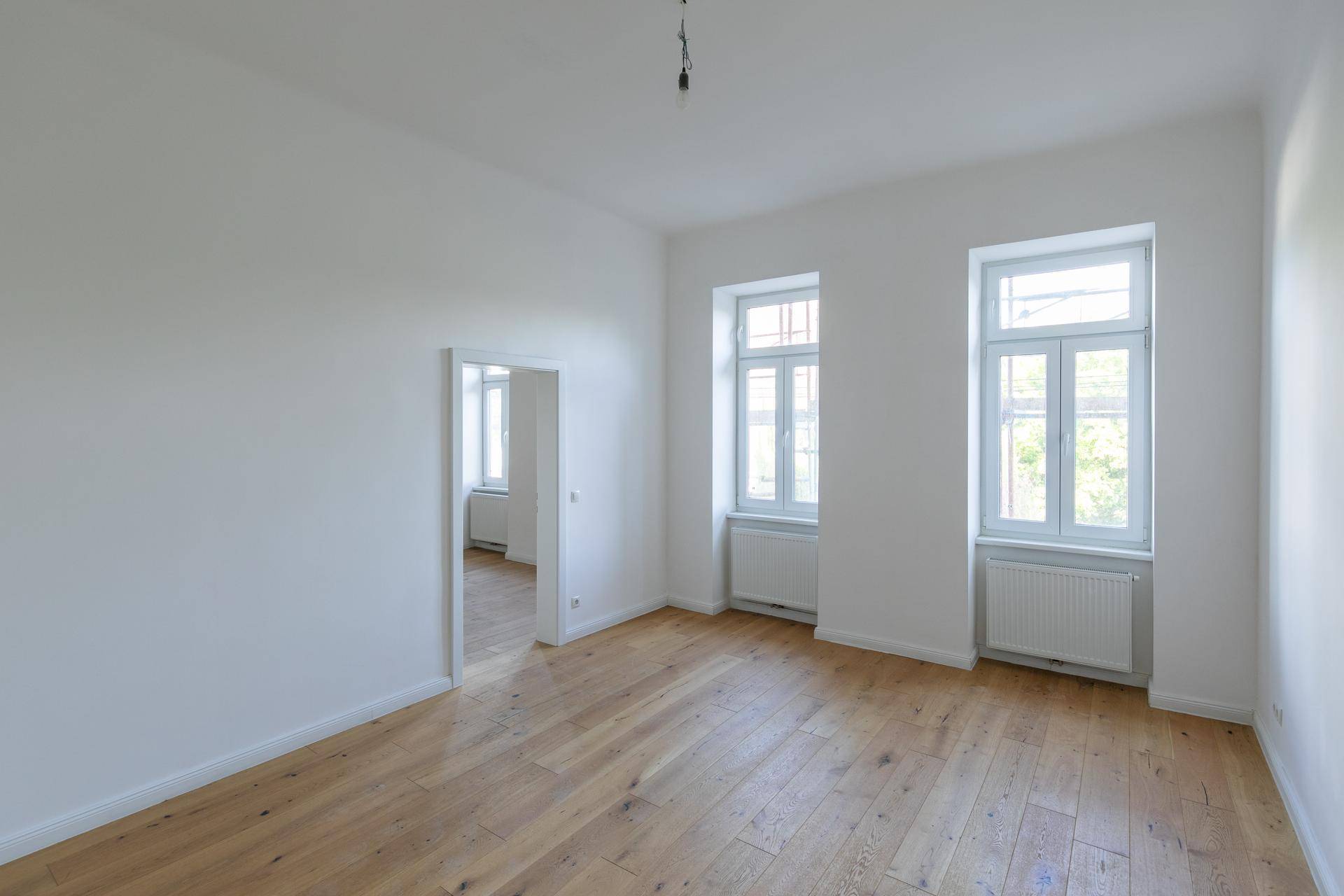 Lichtdurchfluteter Raum mit zwei Fenstern, Holzboden und frisch gestrichenen Wänden, sehr einladend.