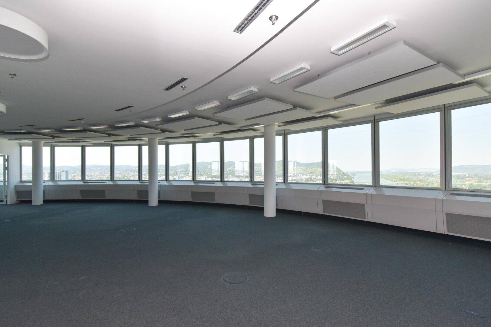 Weitläufiger Bürobereich mit Teppichboden und einer Fensterfront, die einen umfassenden Blick auf die Umgebung bietet.