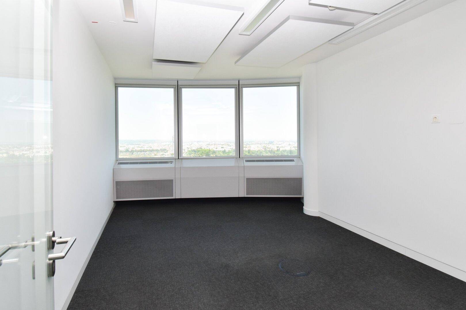 Kleinerer Büroraum mit Teppichboden und großen Fenstern, die einen weiten Blick über die Stadt ermöglichen.