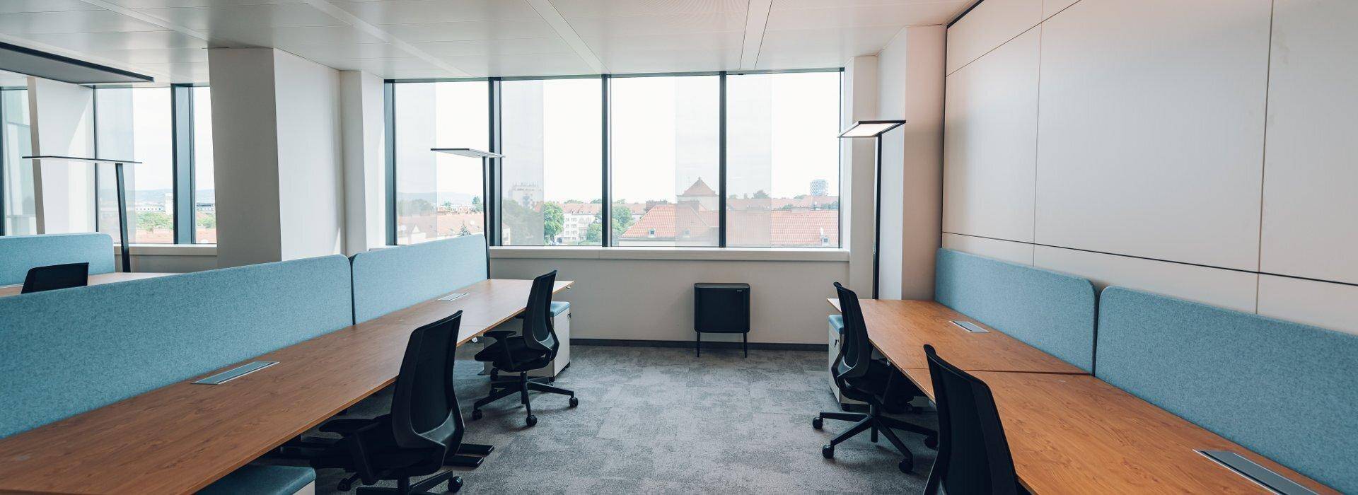 Großes, helles Großraumbüro mit vielen Arbeitsplätzen, großen Fenstern und Teppichboden.