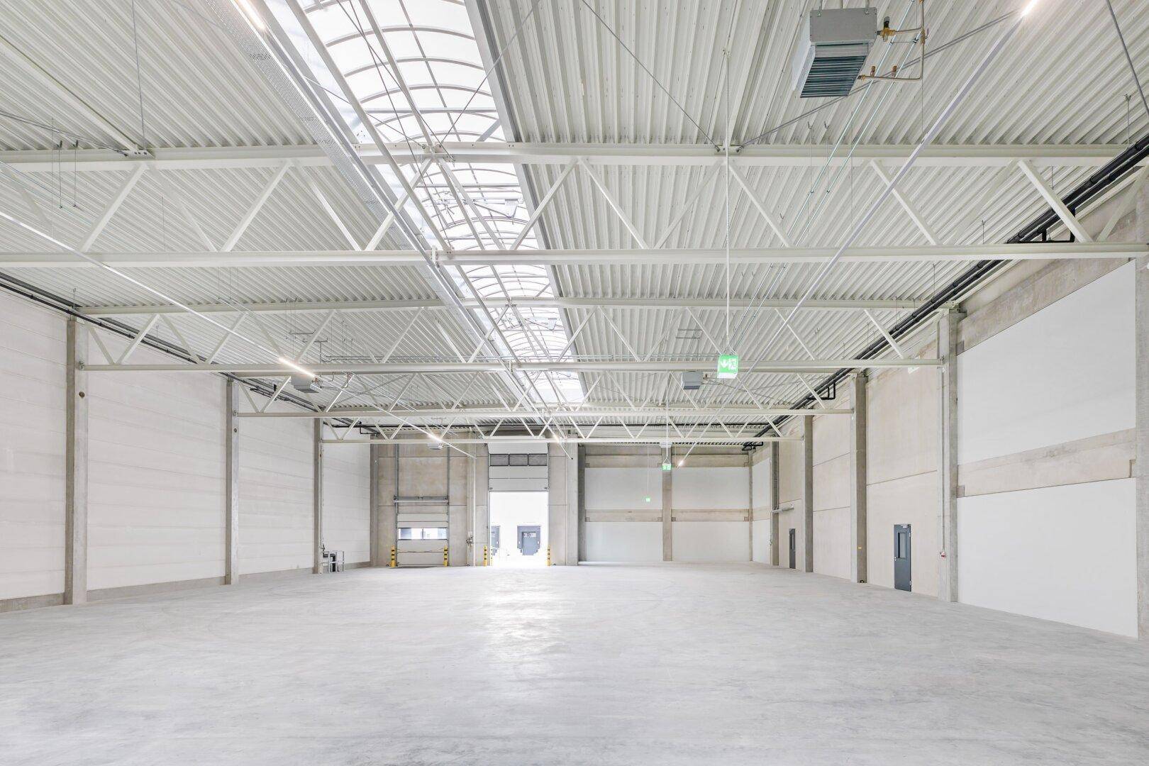 Weitläufige Industriehalle mit hohen Decken, Oberlichtern und großem Rolltor für den Zugang und die Logistik.