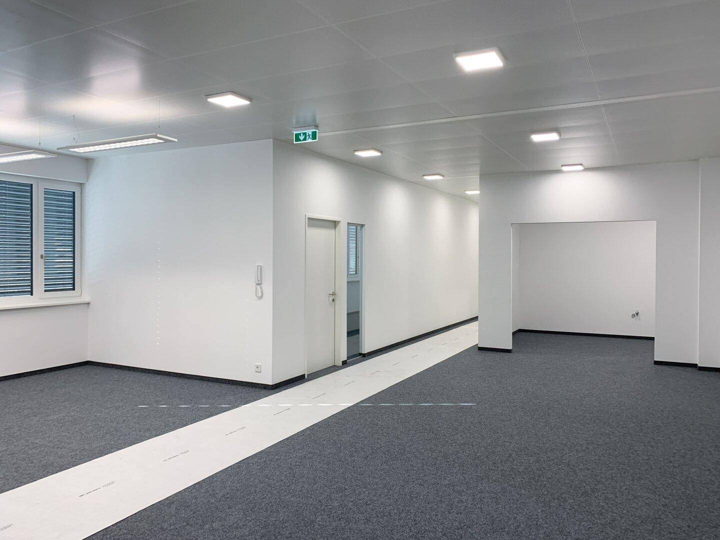 Moderner Bürobereich mit hellem Interieur, grauem Teppichboden und integrierter Beleuchtung, bereit für die Einrichtung.