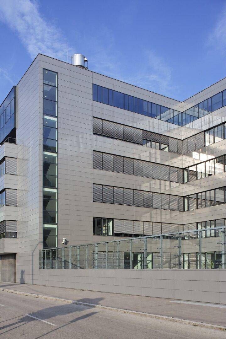 Eckansicht eines modernen Bürokomplexes mit großen Glasflächen und horizontalen Lamellen, die eine dynamische Fassade bilden.