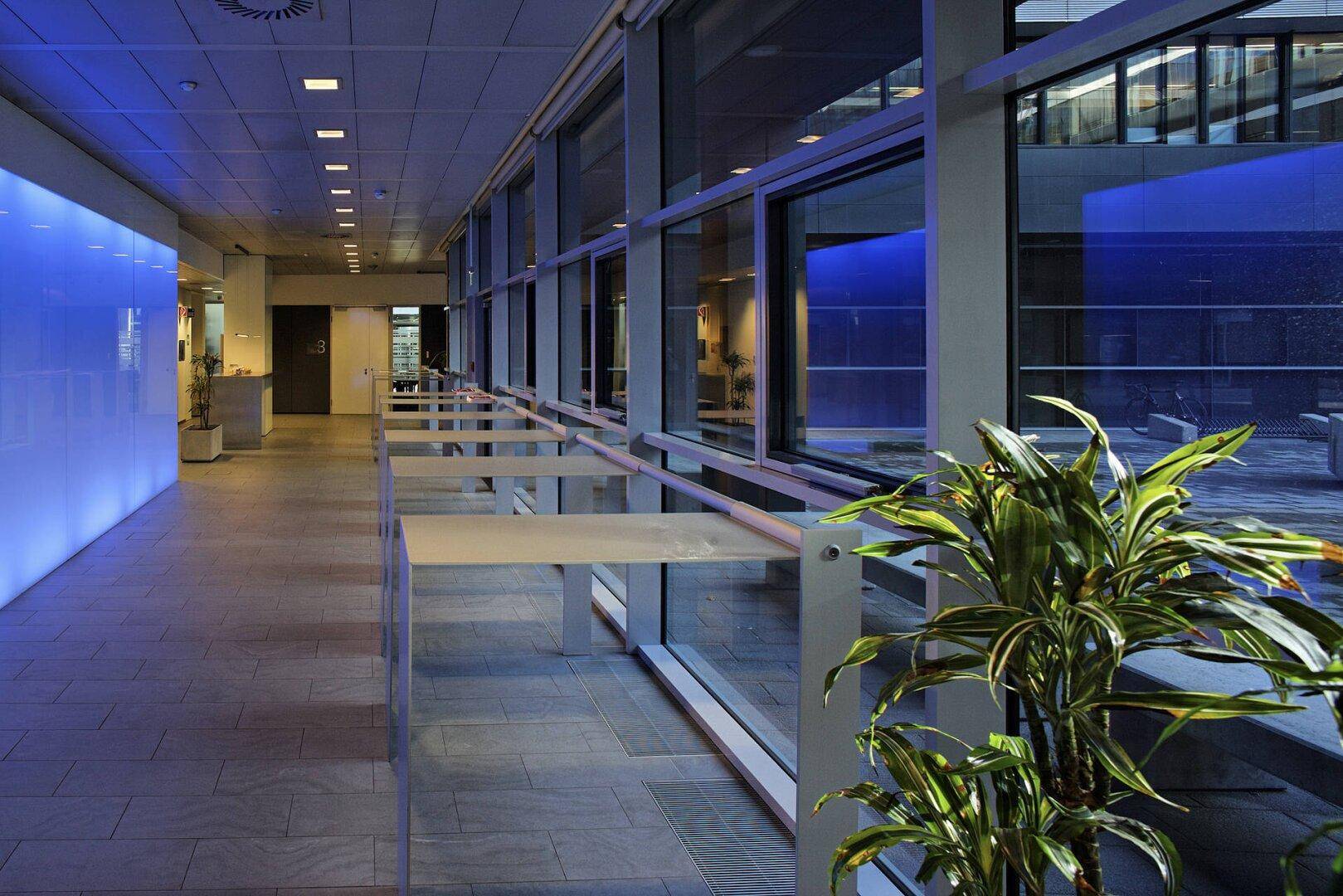 Heller Flur in einem modernen Bürogebäude mit großen Fenstern, die einen Blick auf einen Innenhof ermöglichen.