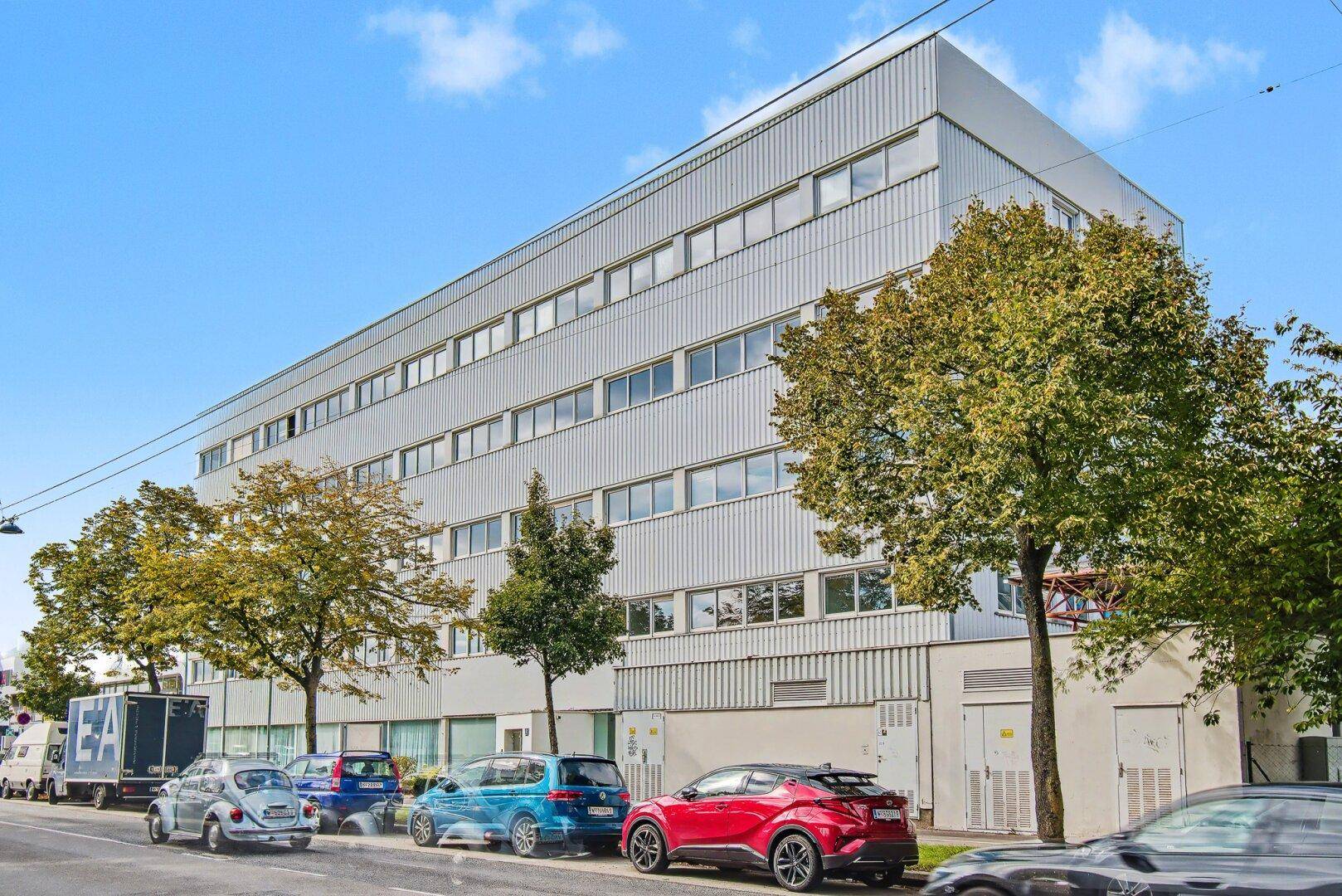 Modernes Bürogebäude mit mehreren Etagen und vielen Fenstern an einer belebten Straße.
