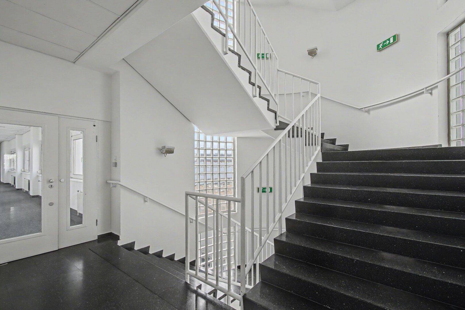 Treppenhaus mit dunklen Stufen, weißem Geländer und Glasbausteinen für natürliches Licht.