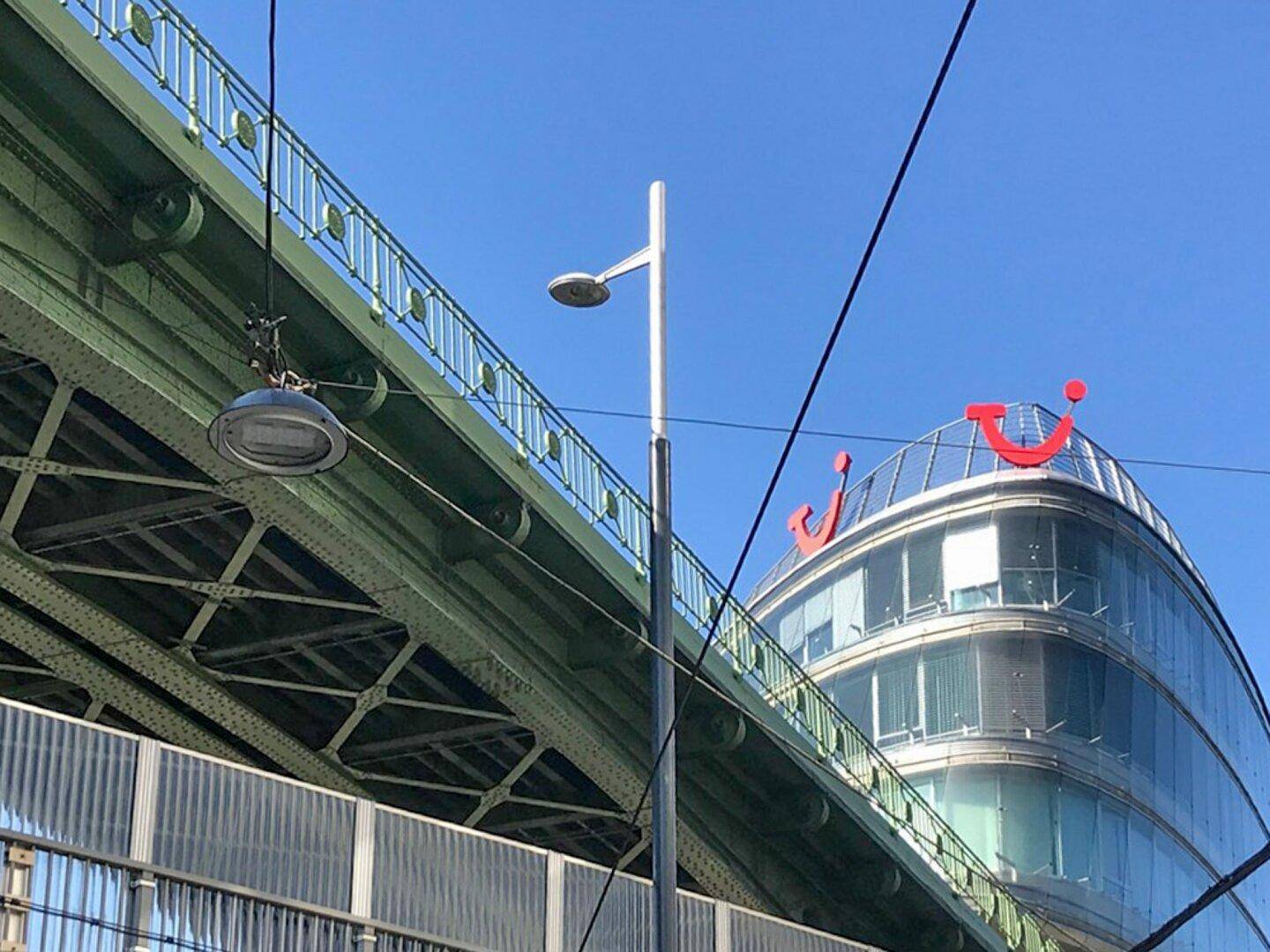Moderne Glasfassade eines Bürogebäudes mit markantem Logo unter einer grünen Stahlbrücke.