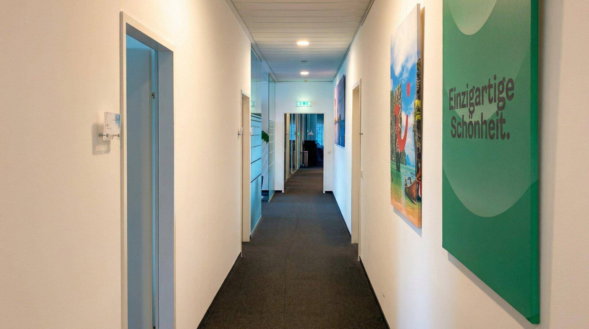 Langer, heller Büroflur mit weißen Wänden, Teppichboden und moderner Beleuchtung.