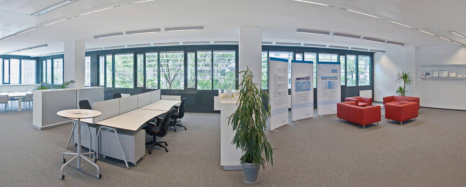 Geräumiges und helles Großraumbüro mit modernen Arbeitsplätzen, einem Loungebereich und großen Fenstern mit Grünblick.