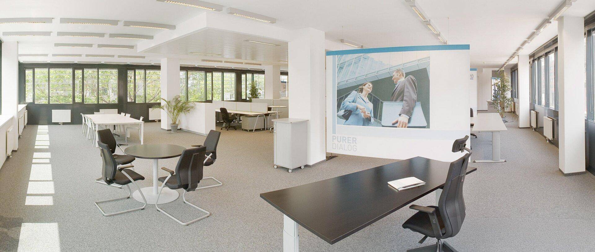 Helles und offenes Büro mit flexiblen Arbeitsbereichen, Besprechungstischen und großen Fenstern für viel Tageslicht.