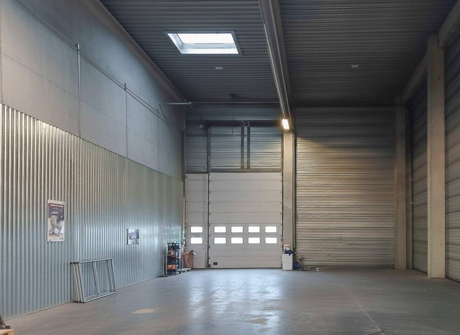 Geräumige Lagerhalle mit hohen Decken, Rolltoren und Oberlicht für Tageslicht.