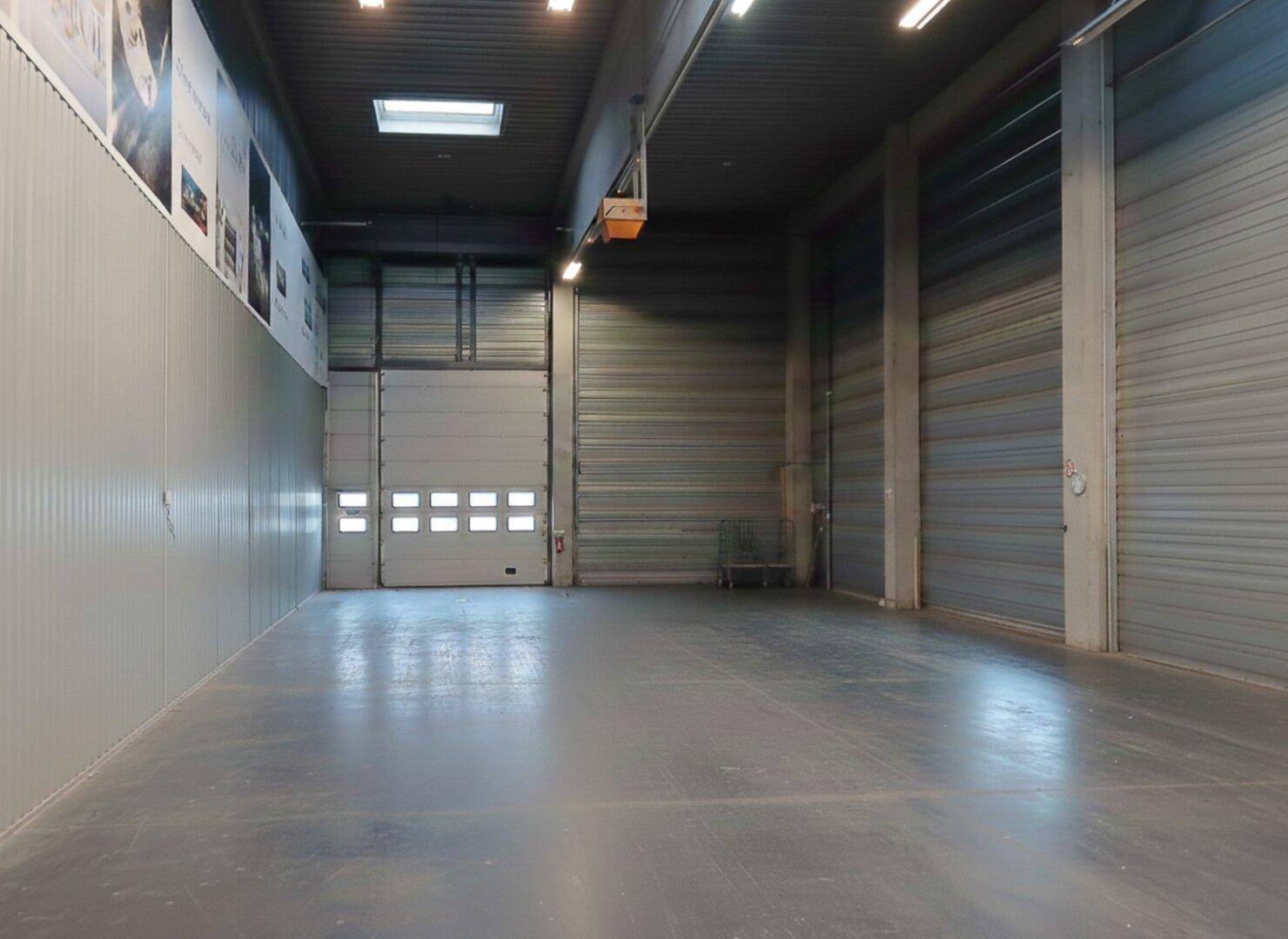 Weitläufige Lagerhalle mit hohen Decken, mehreren Rolltoren und robustem Betonboden, ideal für industrielle Nutzung.