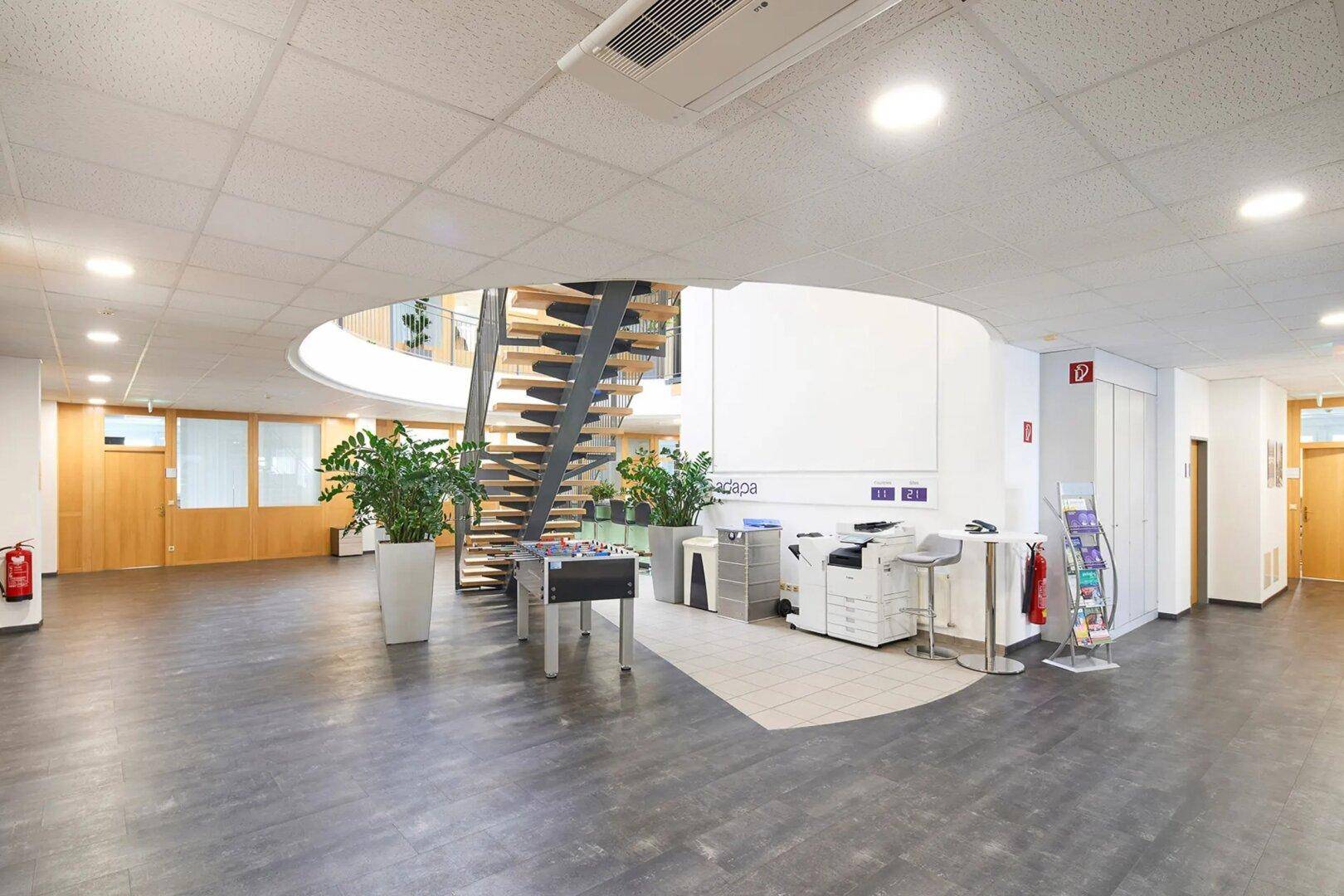 Geräumiger Empfangsbereich mit moderner Wendeltreppe, Foosball-Tisch und Druckerstation.