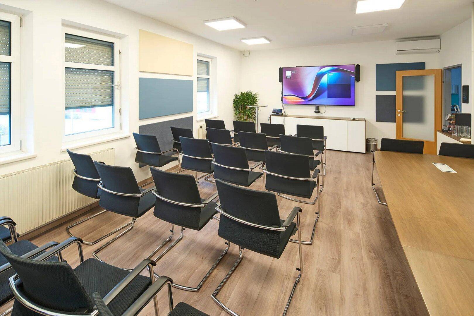 Moderner Konferenzraum mit bequemen Stühlen, einem großen Bildschirm und schallabsorbierenden Paneelen für optimale Akustik.