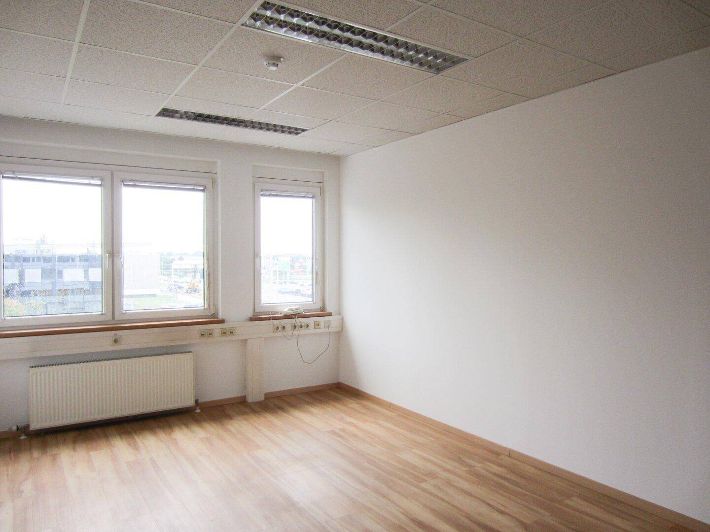 Geräumiges, leeres Büro mit Laminatboden, großen Fenstern und Blick auf die Umgebung, ideal für Arbeitsplätze.