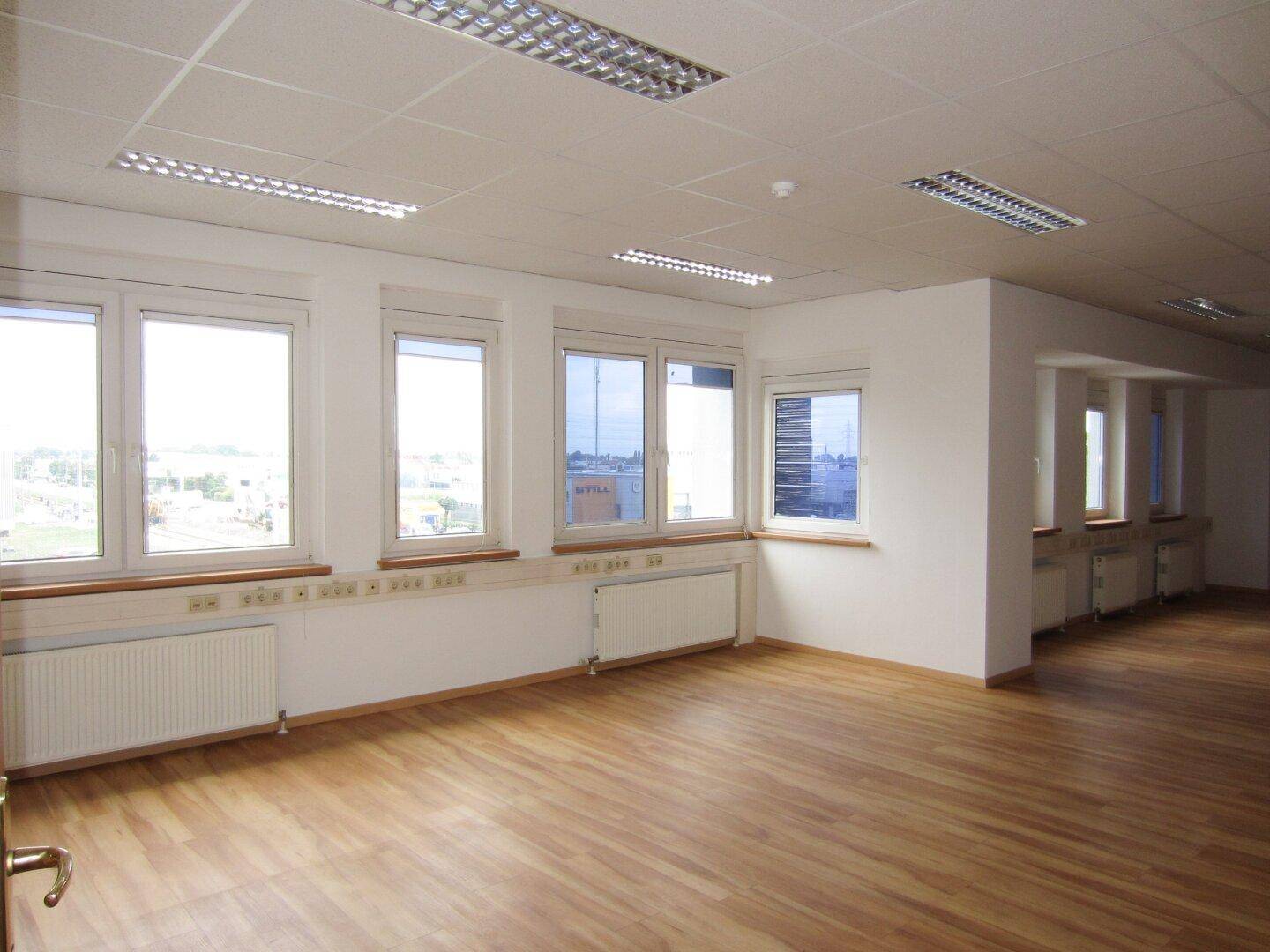 Großes, helles Büro mit Laminatboden, vielen Fenstern und Blick auf die Umgebung, ideal für Großraumbüros.