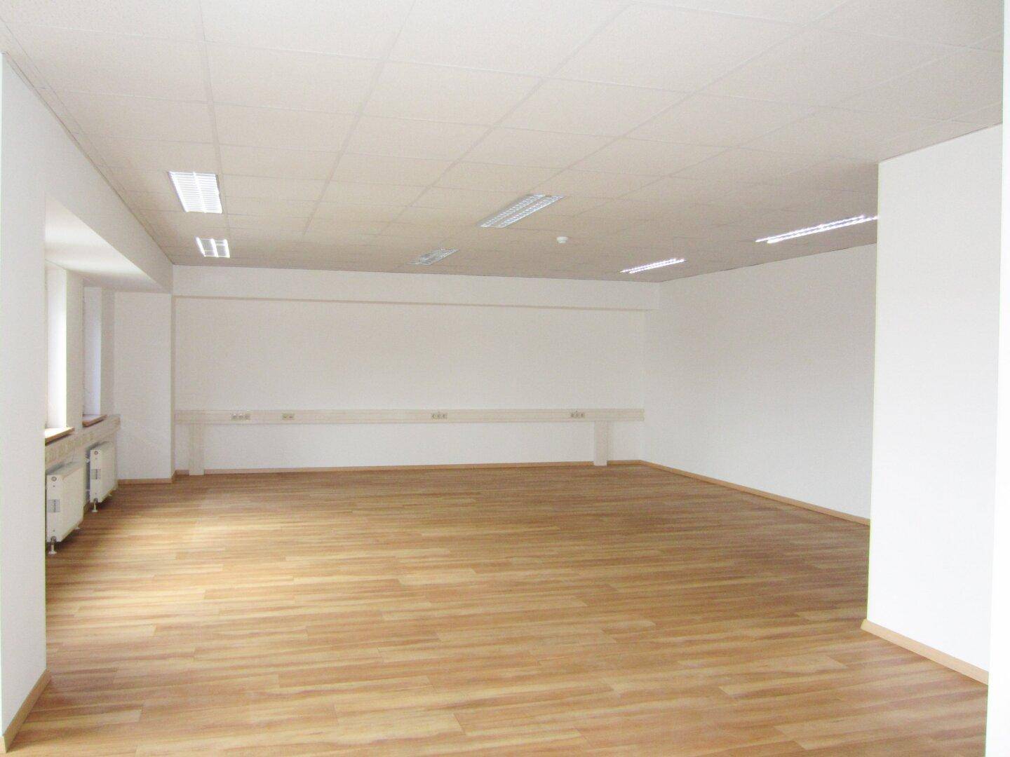 Weitläufiges, leeres Büro mit Laminatboden und weiß gestrichenen Wänden, bereit zur individuellen Gestaltung.