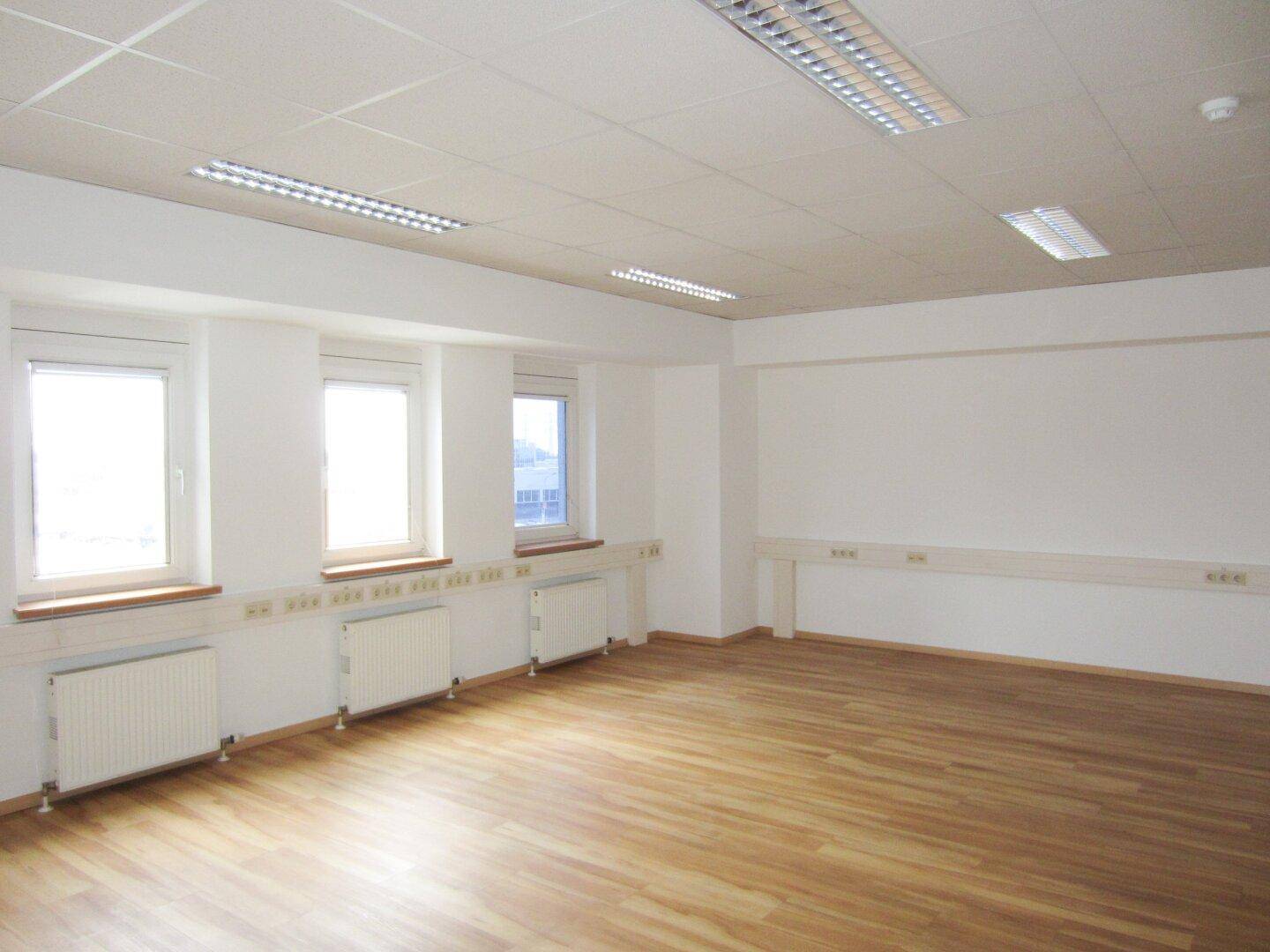 Helles, geräumiges Büro mit Laminatboden, mehreren Fenstern und Blick auf die Umgebung, bietet viel Platz.