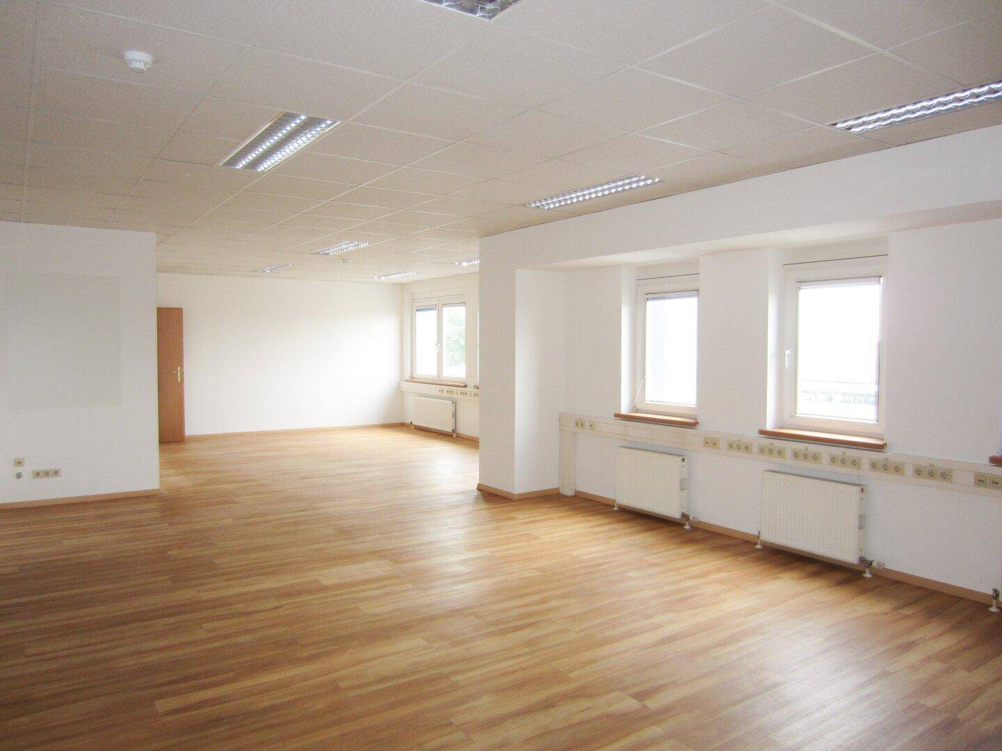 Großes, helles Büro mit Laminatboden, vielen Fenstern und einem offenen Grundriss, ideal für flexible Nutzung.