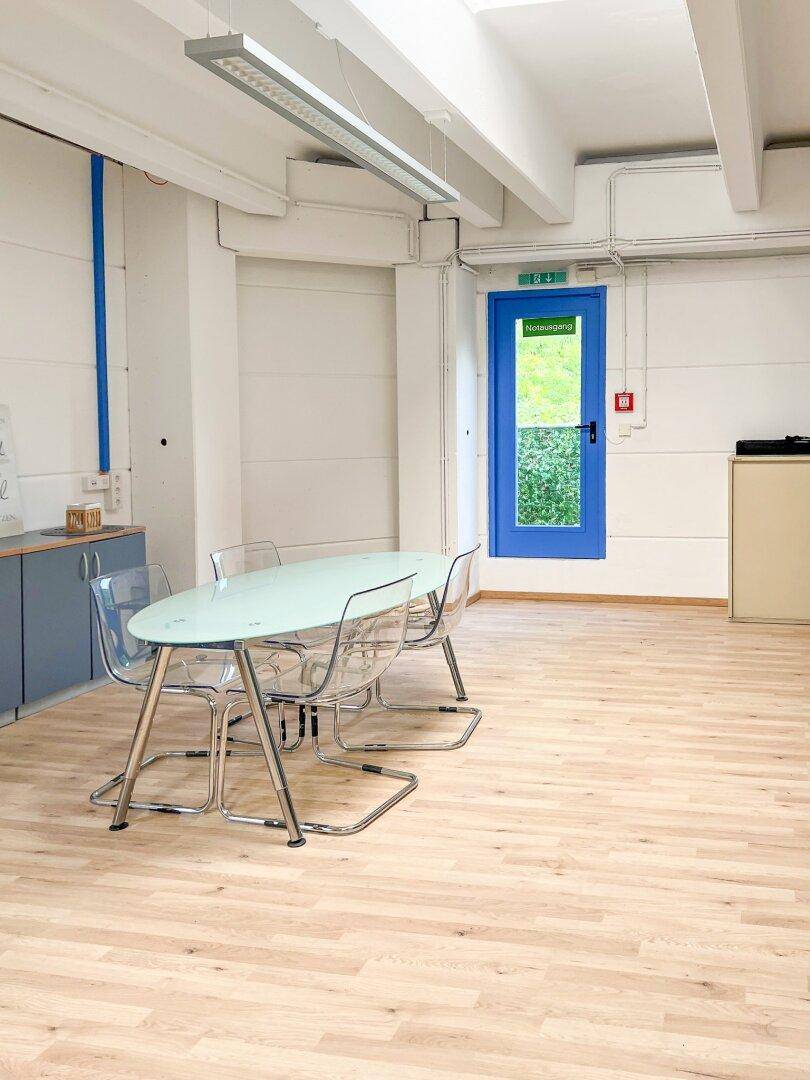 Moderner Besprechungsbereich im Büro mit ovalem Glastisch und transparenten Stühlen.