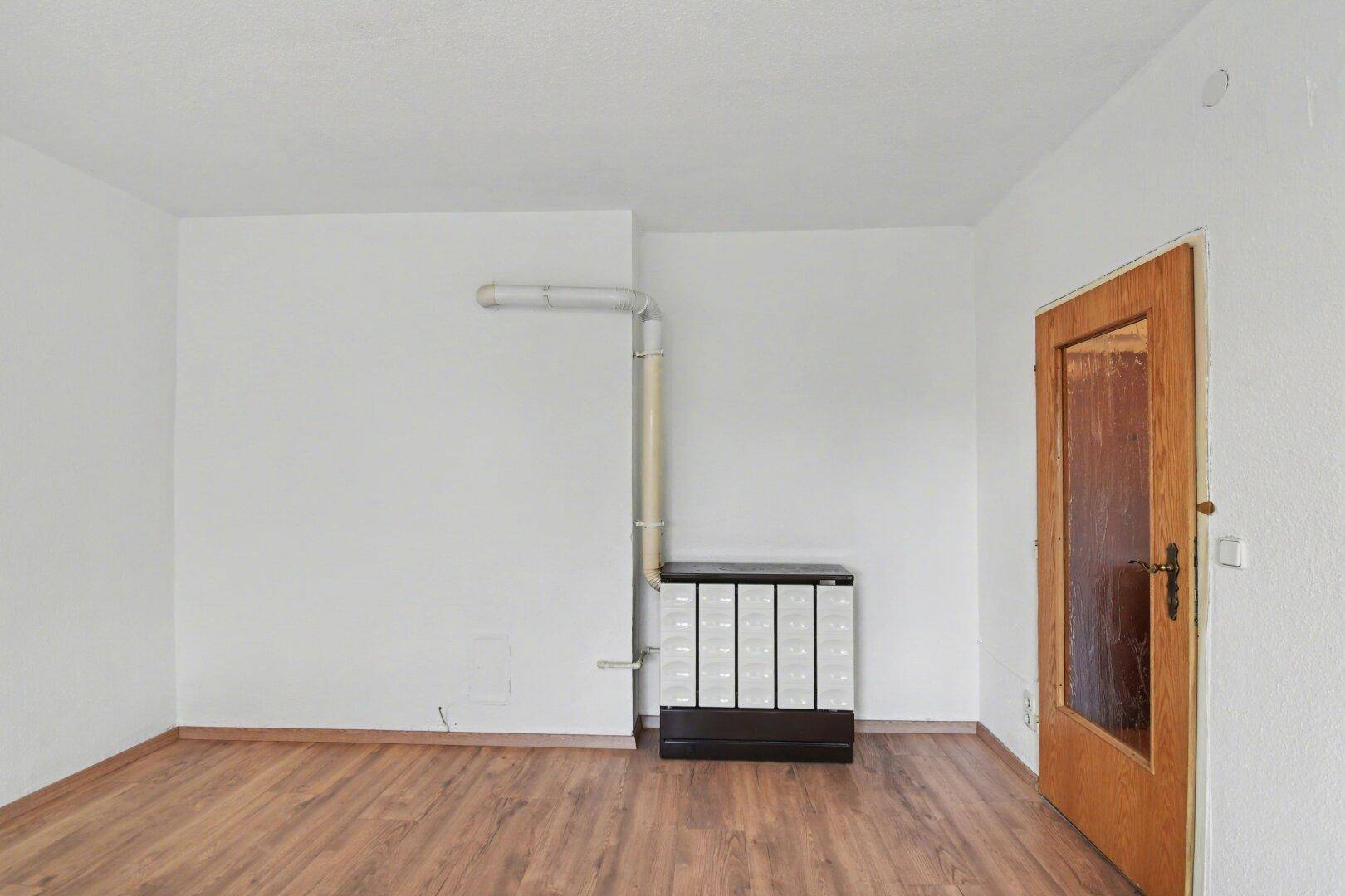 Leerer Raum mit Laminatboden und einem traditionellen Ofen als Heizquelle an der Wand.