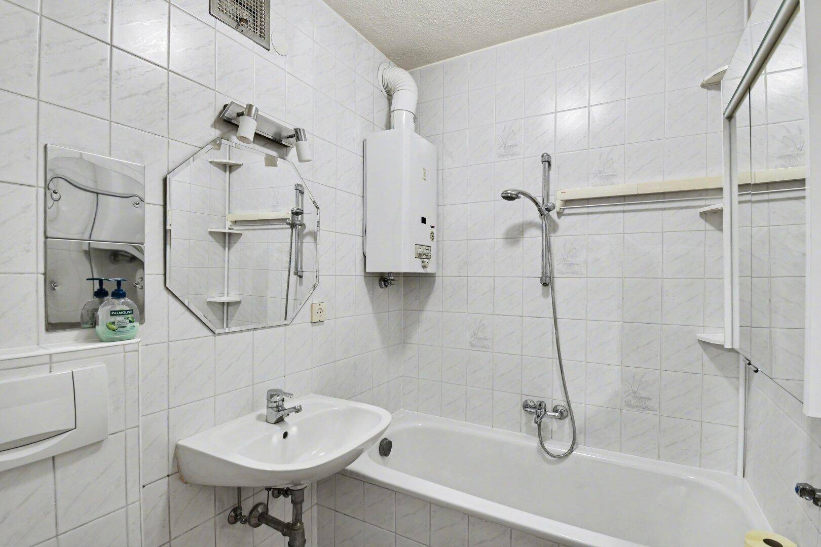 Gefliestes Badezimmer mit Badewanne, Waschbecken und einem Gas-Durchlauferhitzer an der Wand.