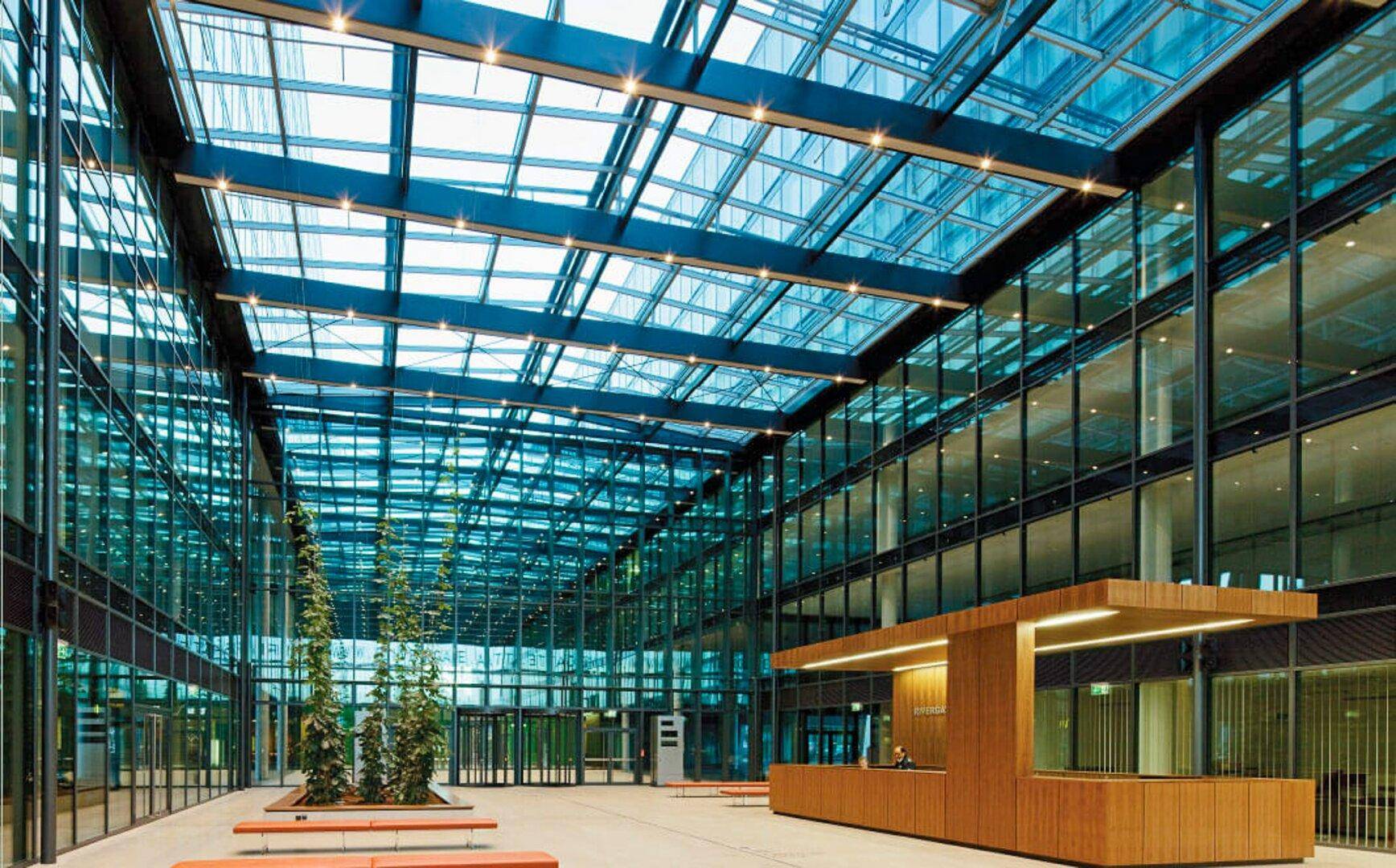 Großzügige, moderne Lobby mit Glasdach, viel Tageslicht und einer eleganten Holzrezeption.