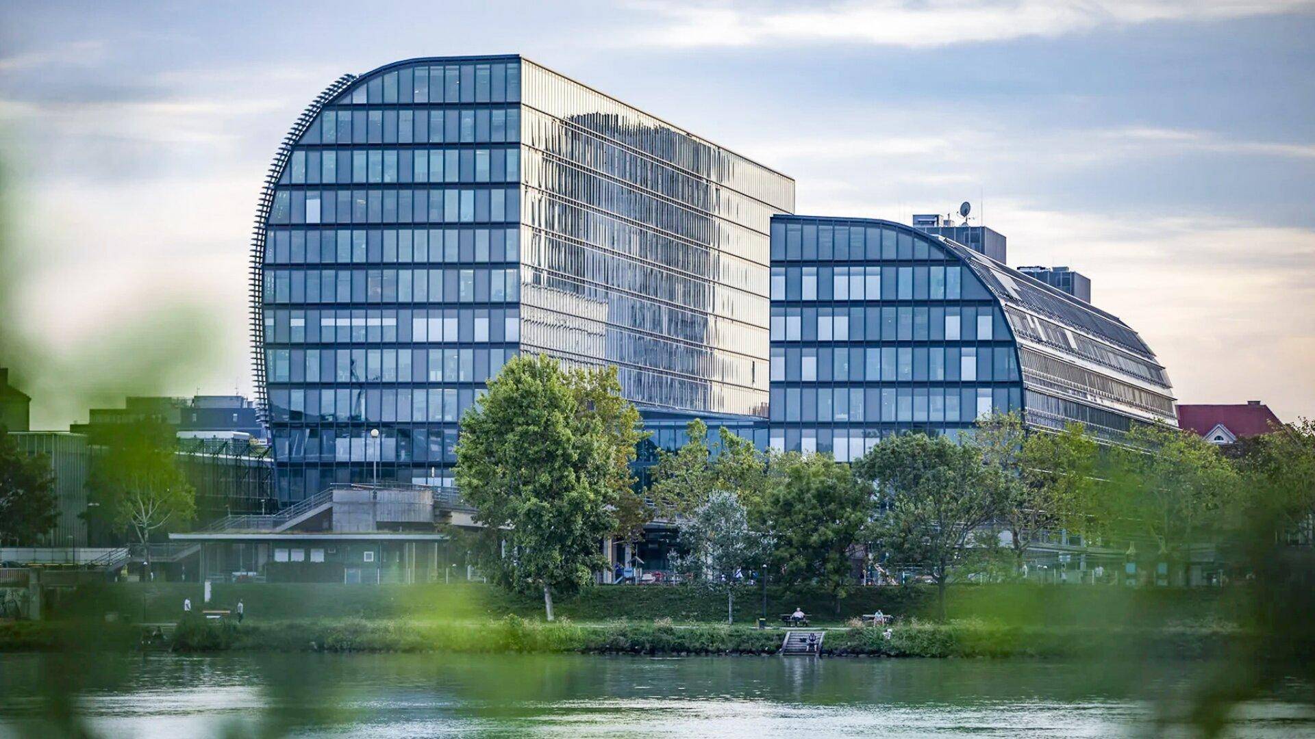 Beeindruckendes modernes Gebäude mit geschwungener Glasfassade, gelegen an einem Gewässer.