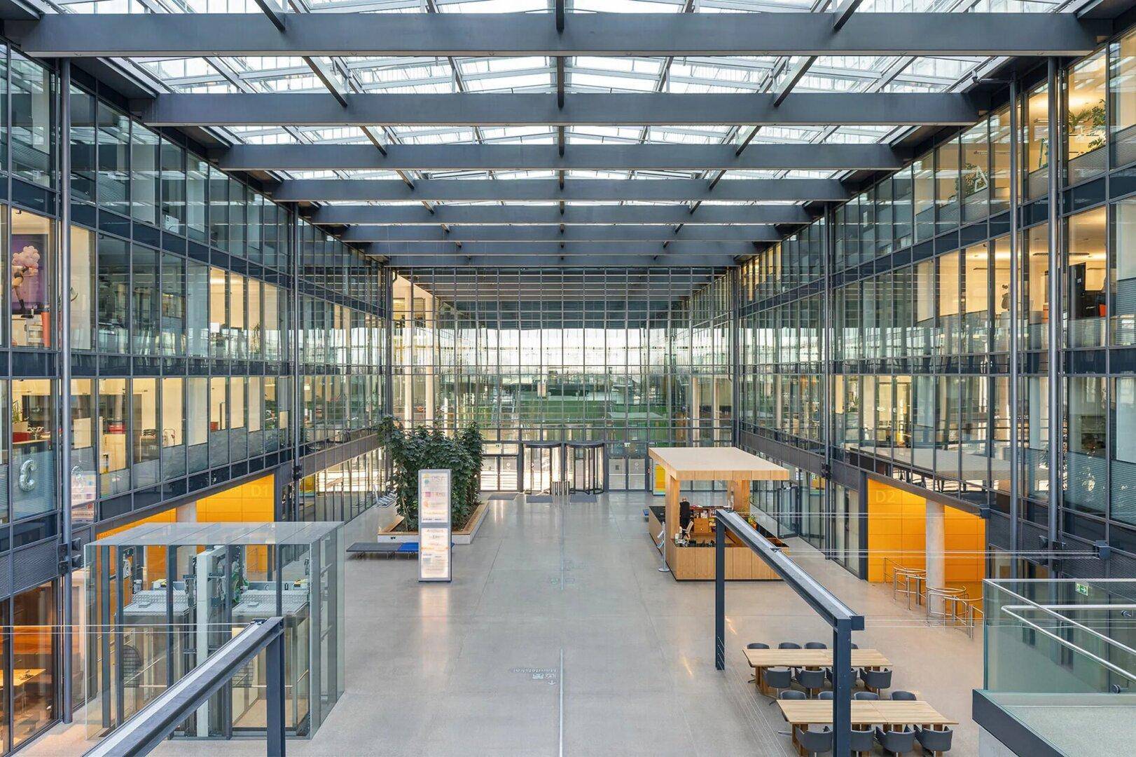 Großes, modernes Atrium mit Glasfassade und hohen Decken, das viel natürliches Licht in die Büroetagen lässt.