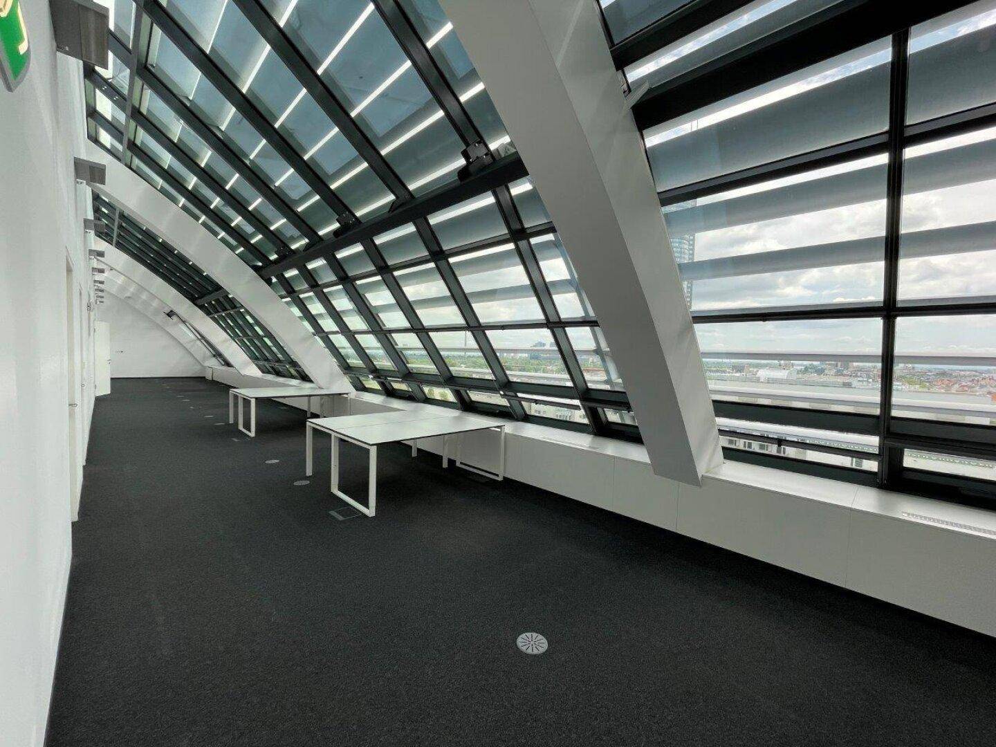 Heller Büroraum im Dachgeschoss mit schrägen Glasfenstern und weitem Blick über die Stadt, ideal für kreative Arbeitsbereiche.