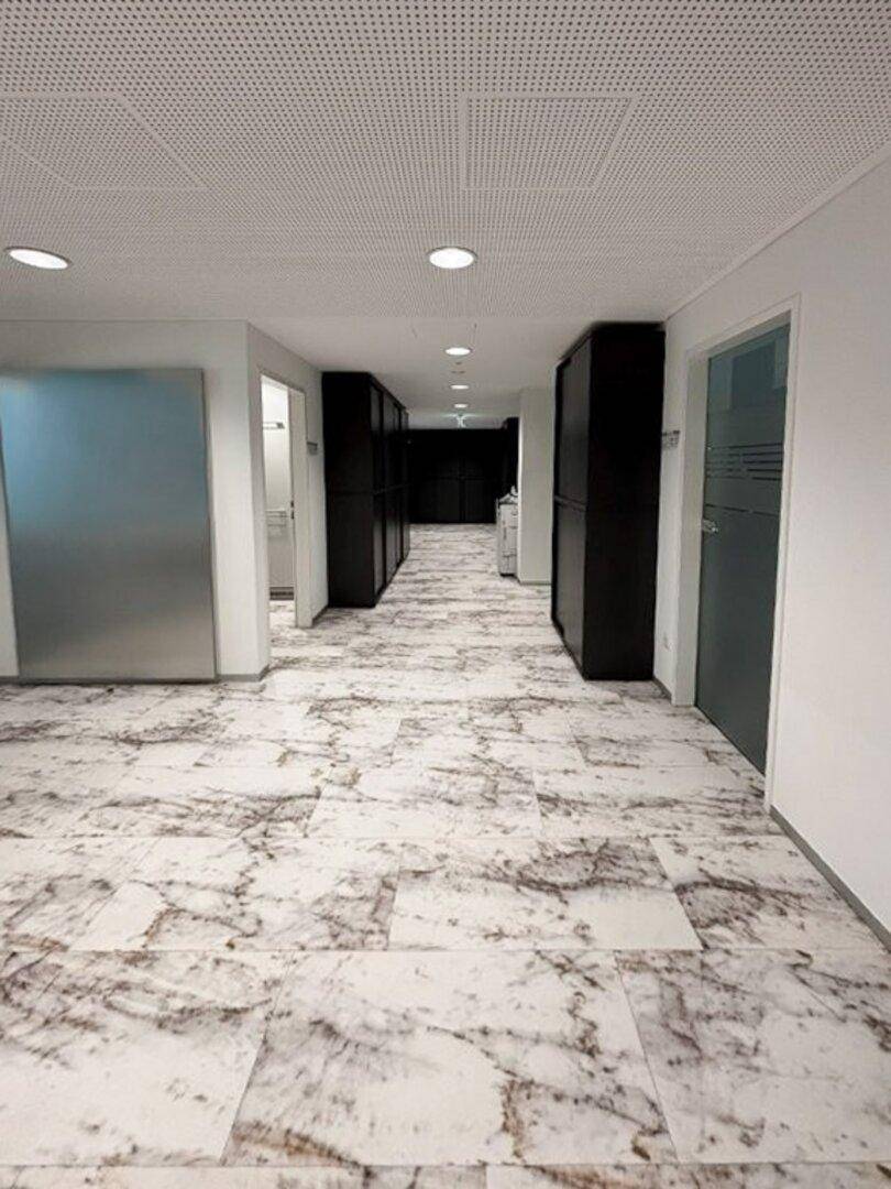 Heller Flur mit elegantem Marmorboden und dunklen Schränken, der zu Büros und Arbeitsbereichen führt.