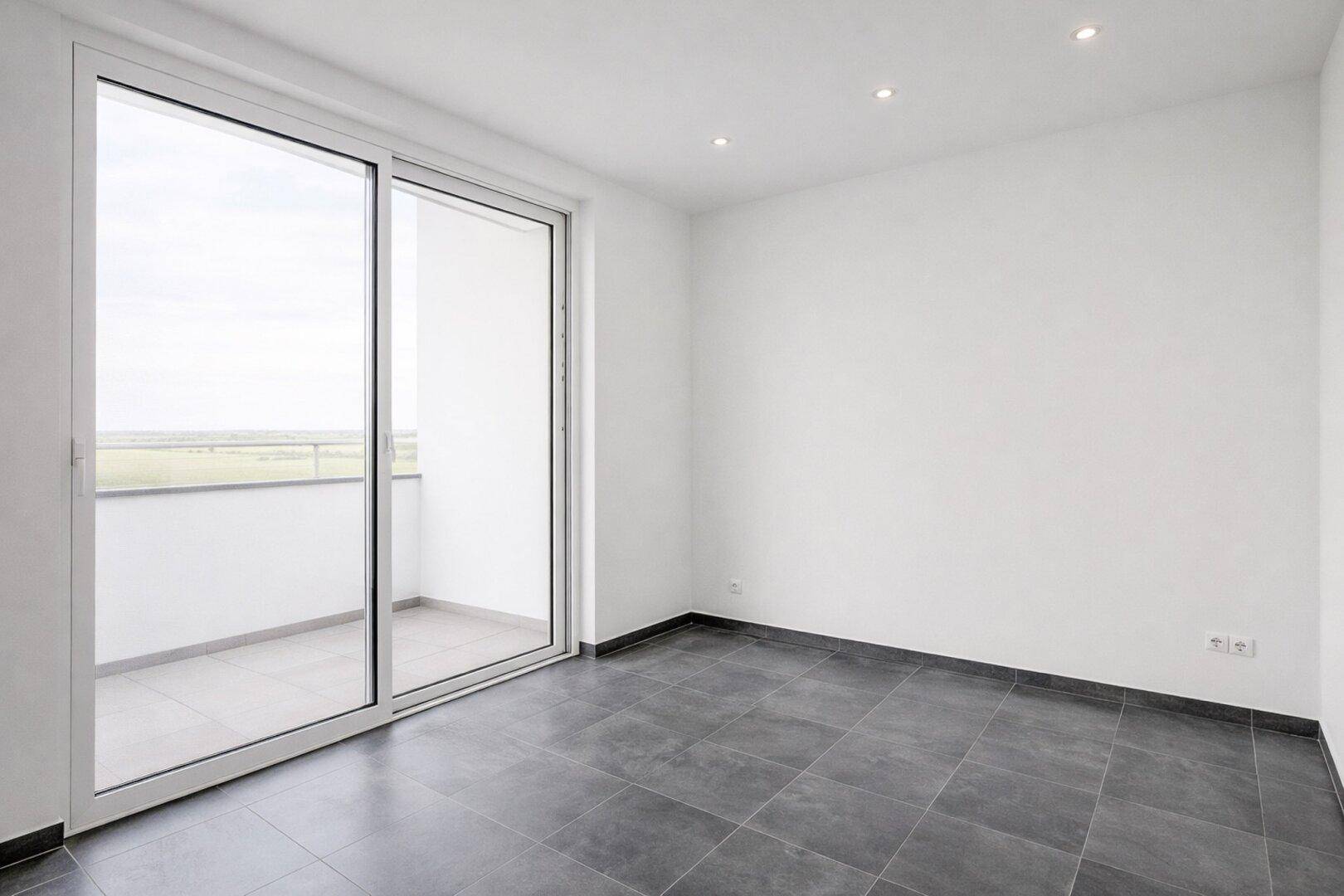 Heller Raum mit großen Schiebetüren zum Balkon und dunklen Fliesen auf dem Boden.