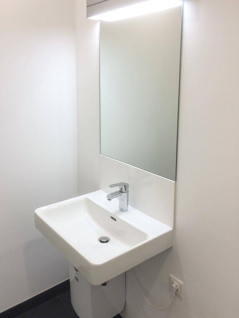 Modernes Gäste-WC mit weißem Waschbecken, Spiegel und schlichter Beleuchtung.