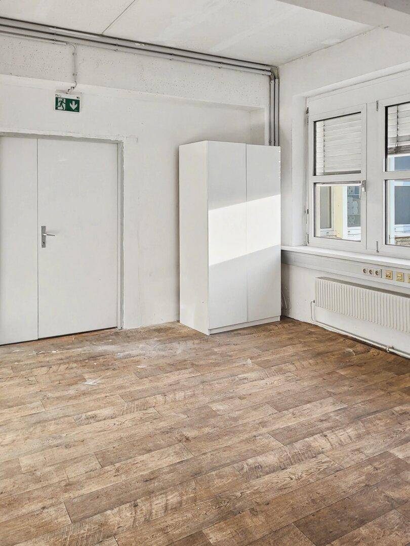 Raum mit Holzplankenboden, weißen Wänden, einem weißen Schrank und Fenstern mit Jalousien.