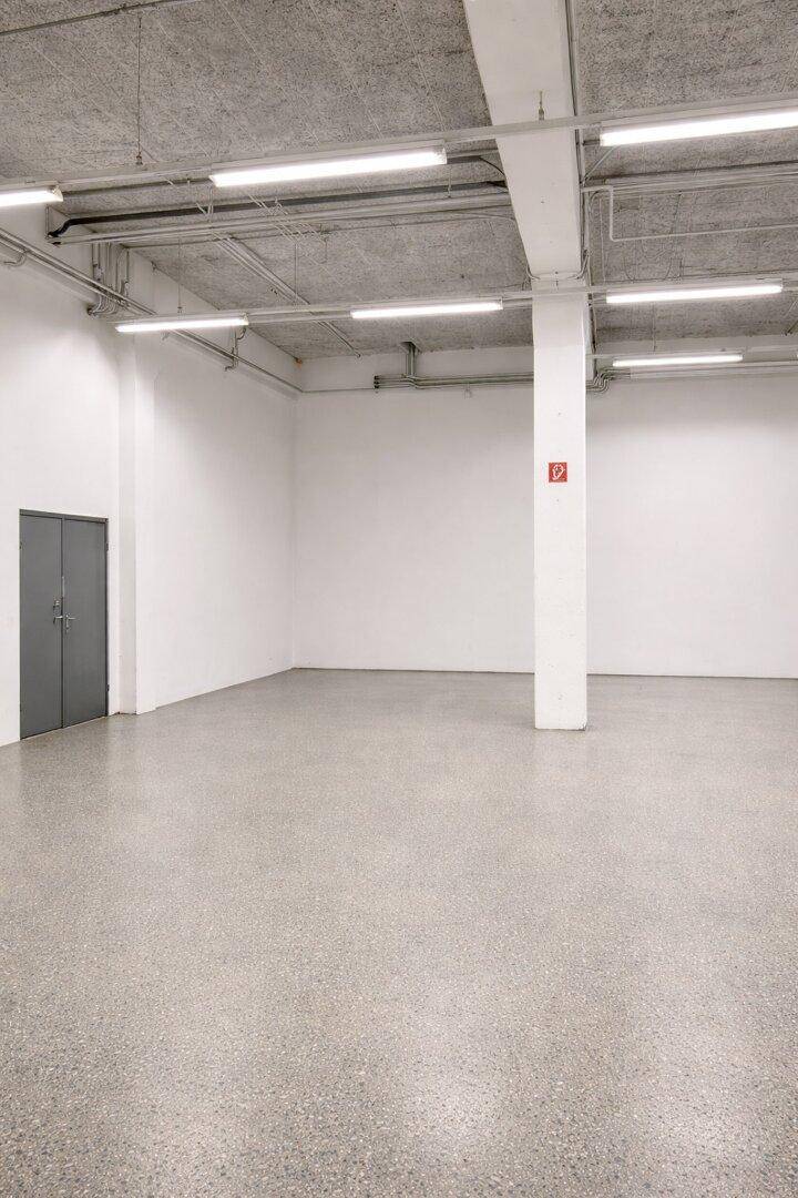 Heller, leerer Gewerberaum mit grauem Terrazzoboden und einer großen Doppeltür.