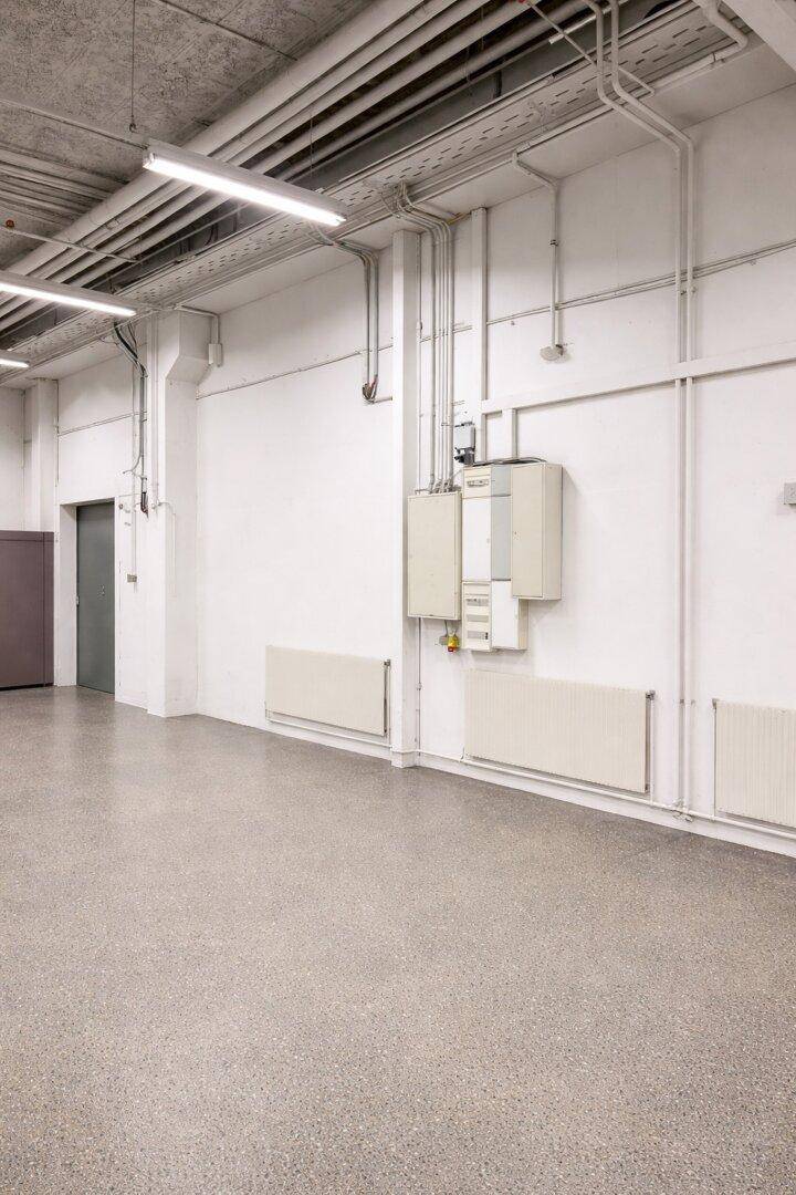 Leerer Gewerberaum mit weißen Wänden, Heizkörpern und sichtbaren Elektroinstallationen an der Wand.
