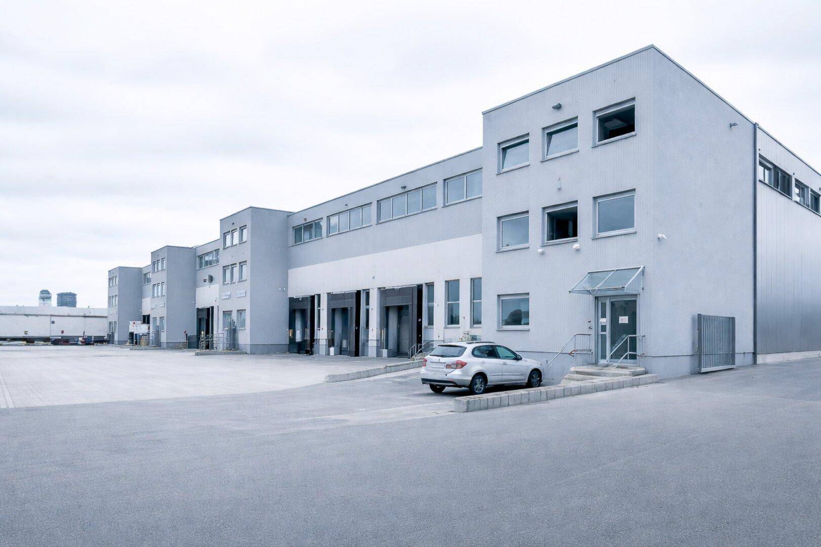 Gewerbegebäude mit mehreren Laderampen und weitläufigem Vorplatz an einem bewölkten Tag.