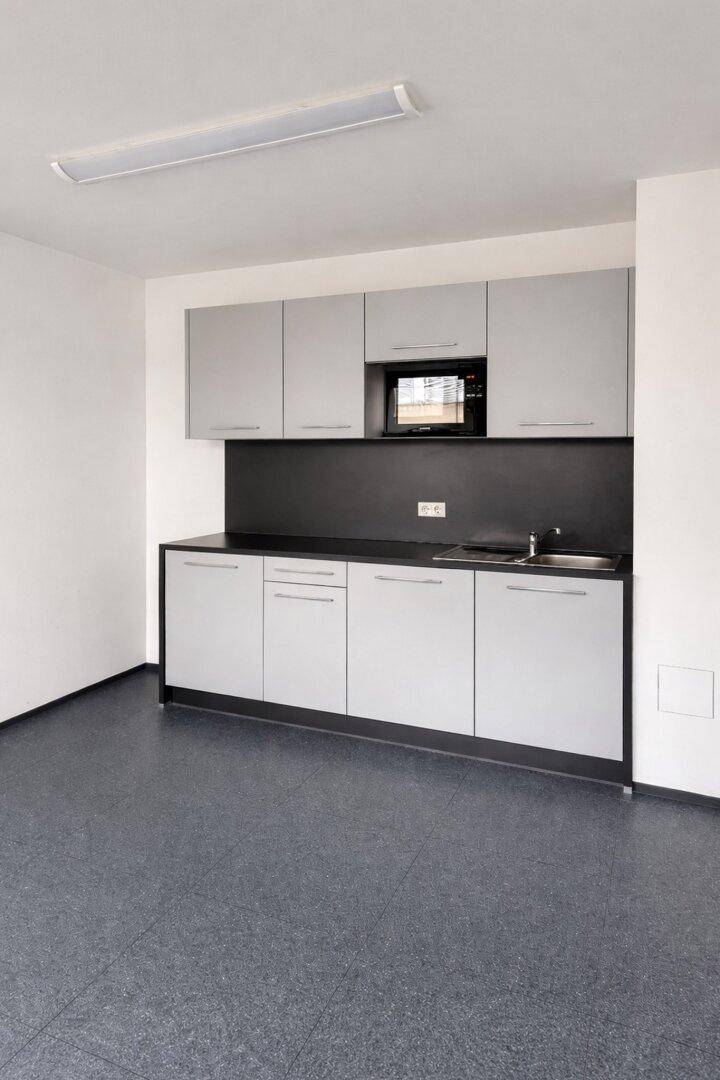Moderne Küchenzeile mit grauen Schränken, dunkler Arbeitsplatte und integrierter Mikrowelle.