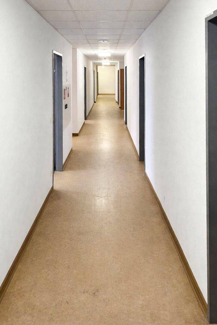 Langer, heller Flur mit mehreren Türen auf beiden Seiten und einem strapazierfähigen Bodenbelag.